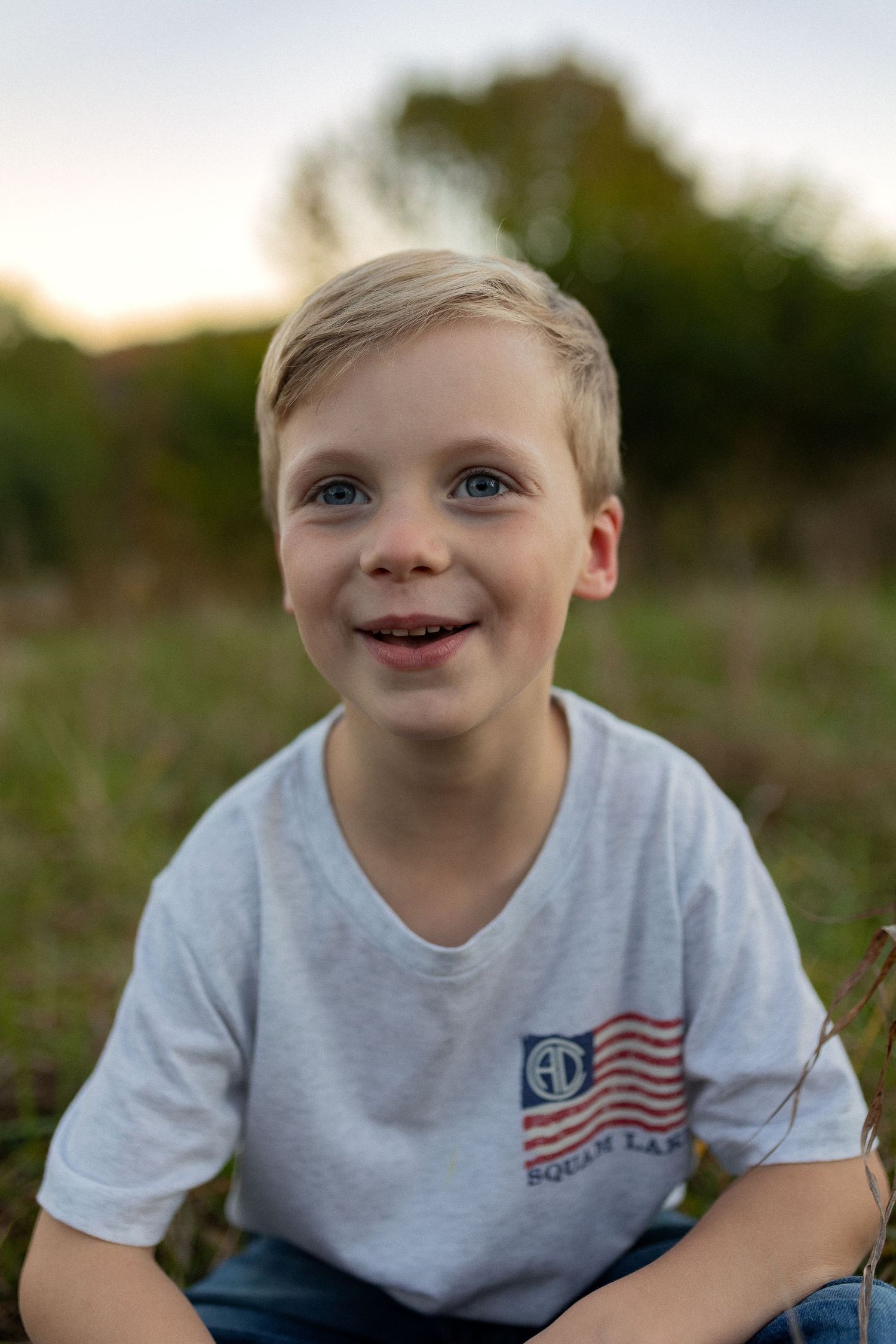 Young person wearing t-shirt with American flag design smiling brightly outdoors.