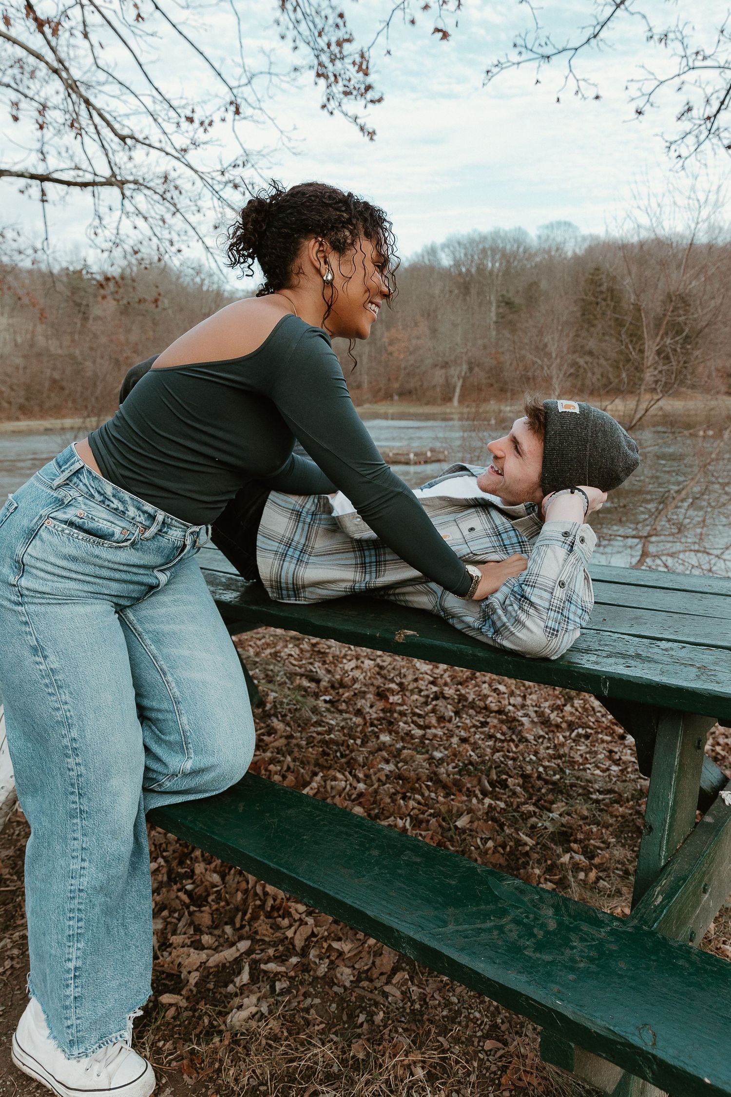 Candid playful couple moment as she leans in across a picnic table, cozy and real with nostalgic film-inspired tones.
