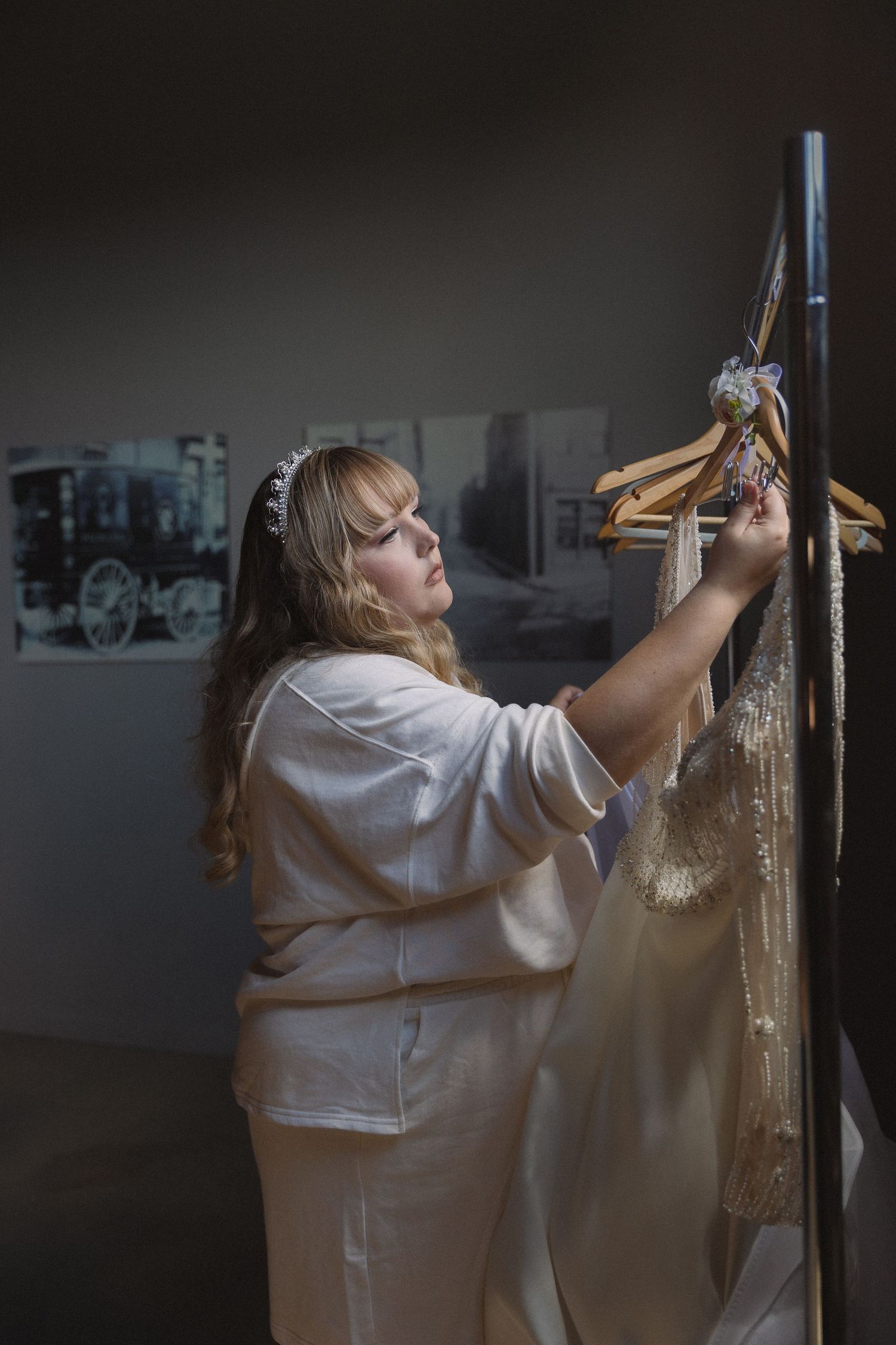 Wedding dress attendant carefully hanging and preparing gown in dimly lit room.