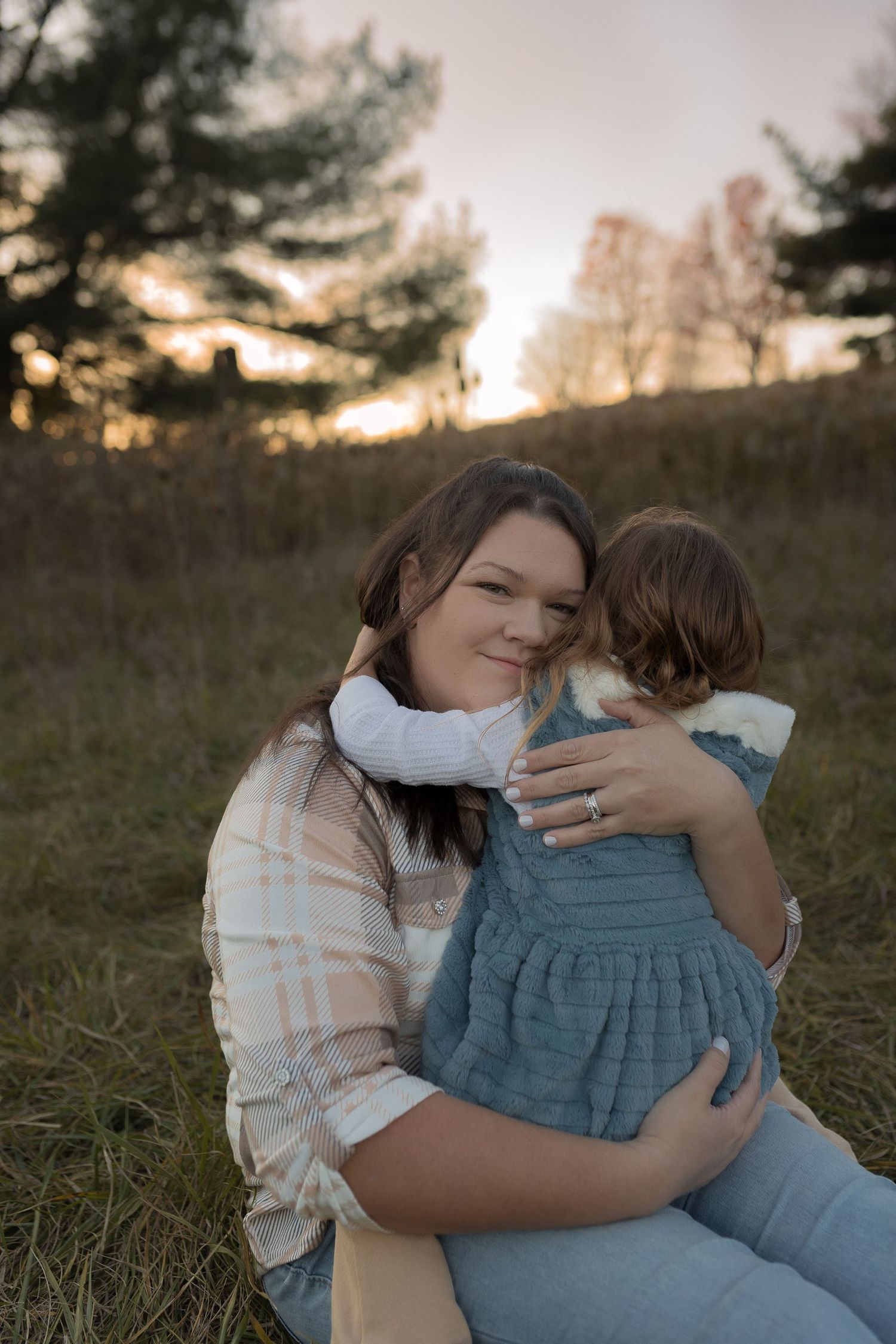 Tender moment between parent and child embracing outdoors during sunset in rural setting.