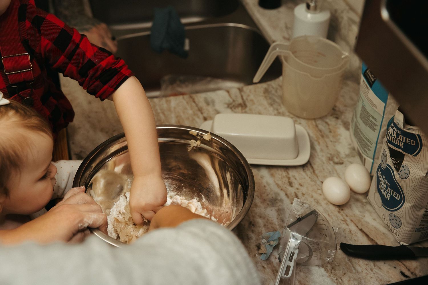 Small hands reaching into a mixing bowl while baking in a kitchen.
