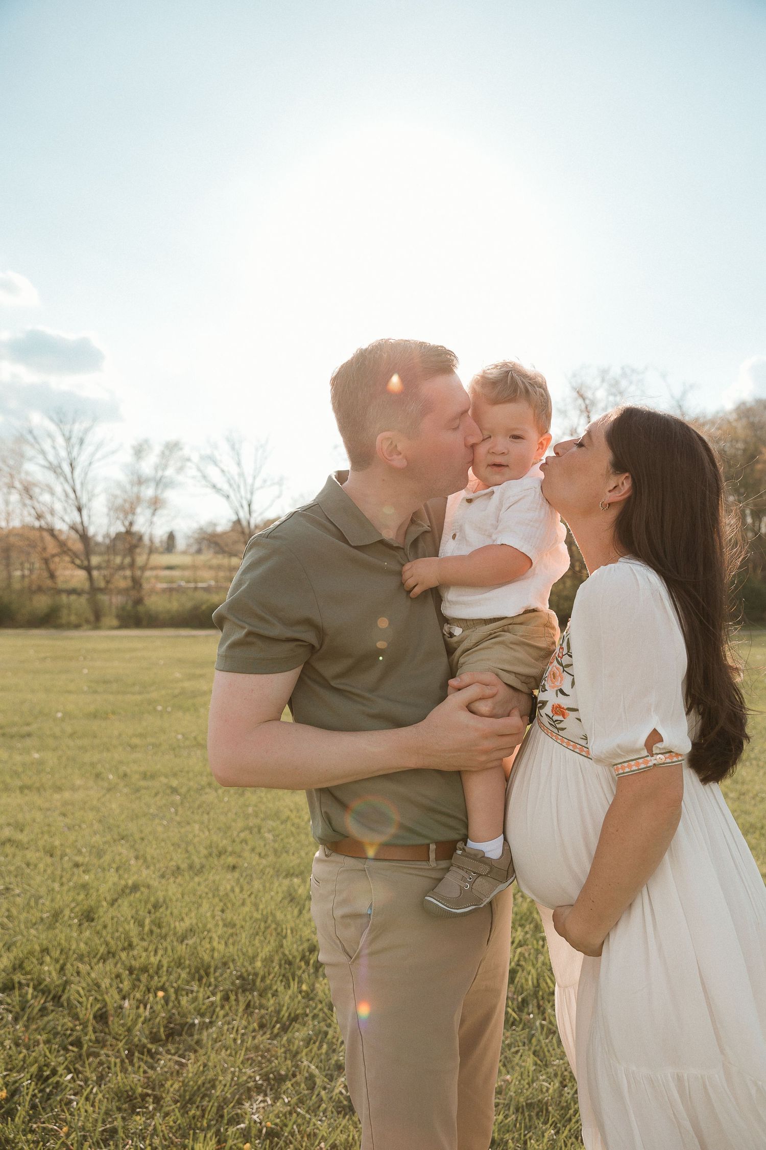 Playful maternity photo of parents lifting toddler in a sunlit field, celebrating love, laughter, and growing family with storytelling edits