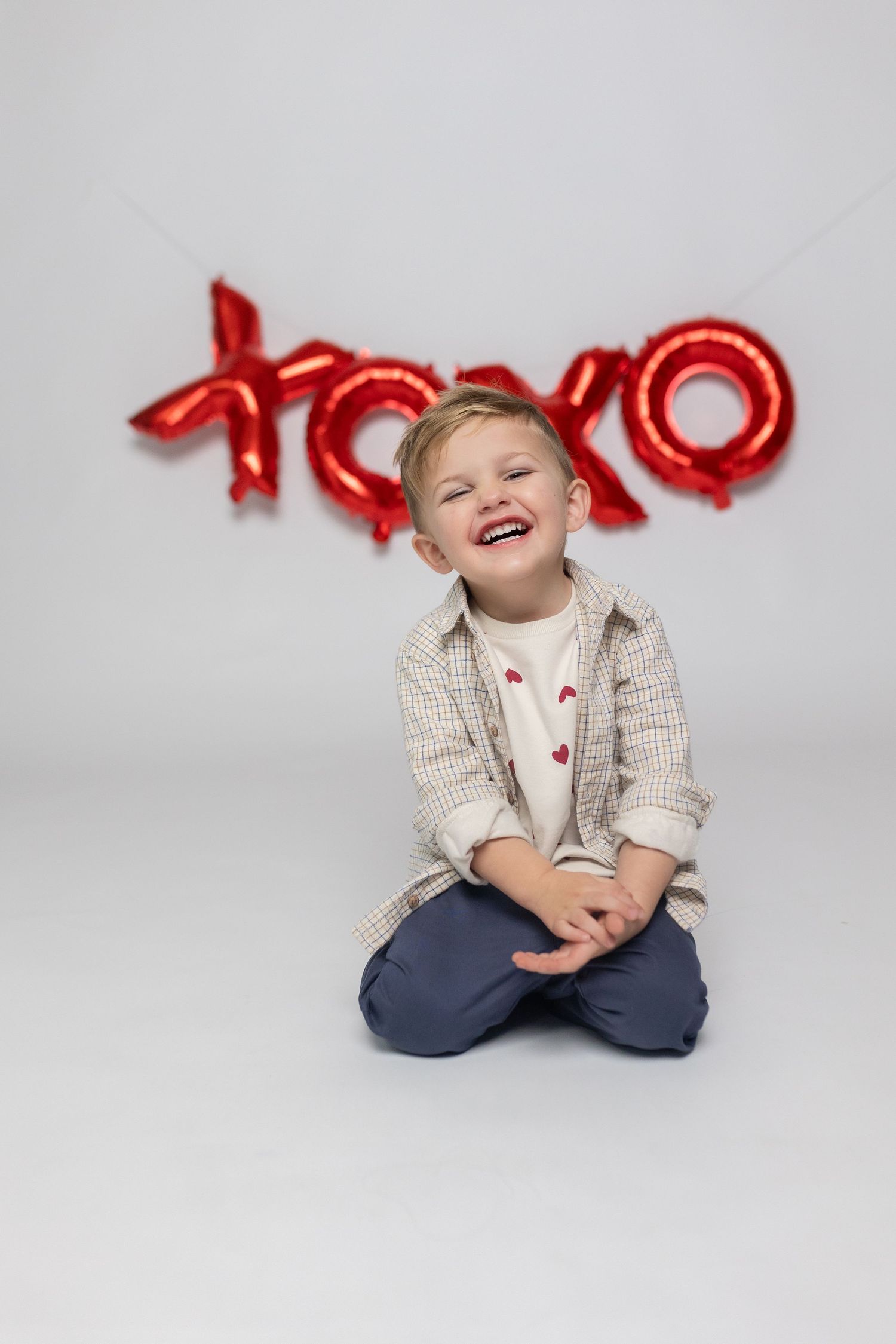 A child sitting cross-legged in casual attire against white background with red balloon letters.
