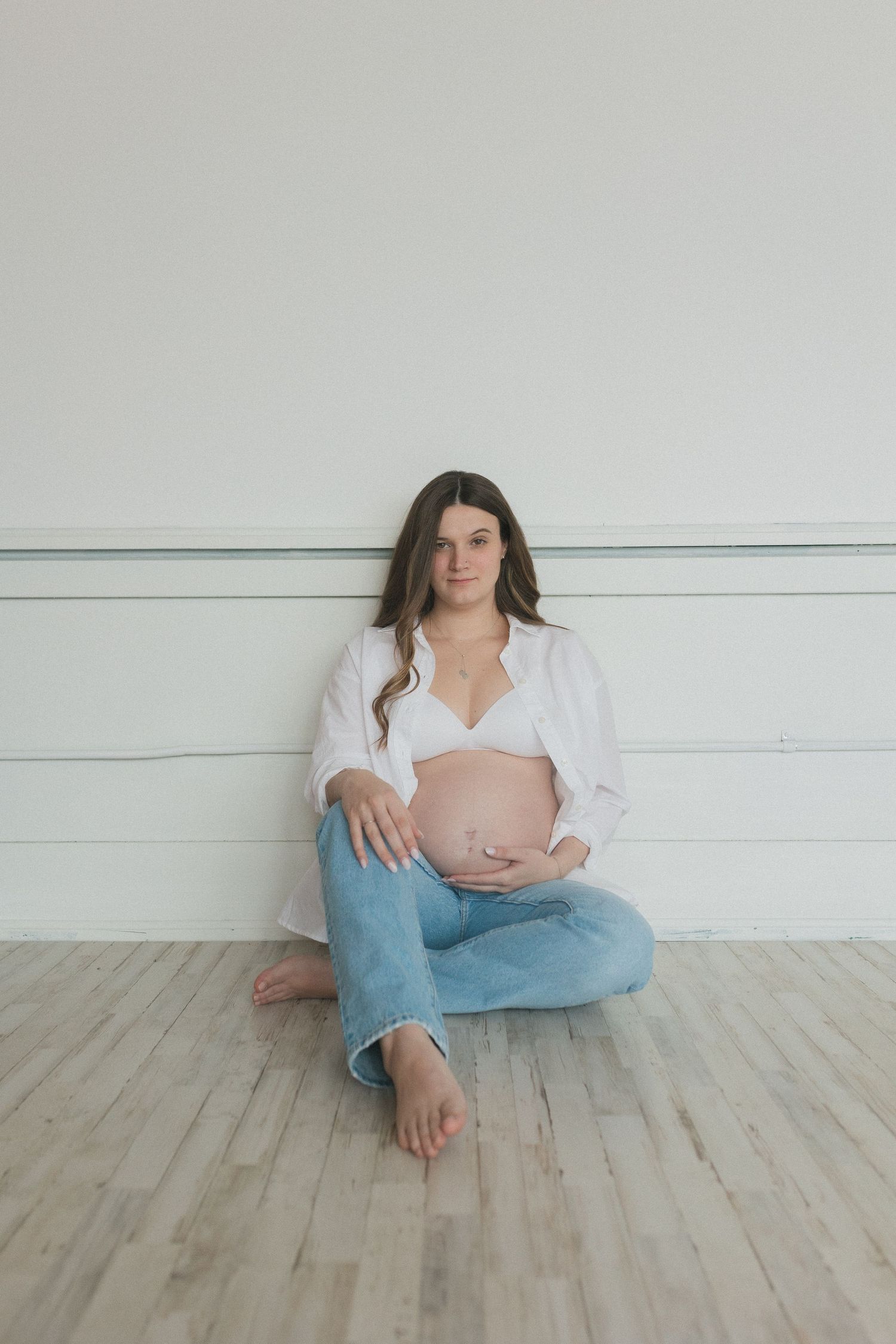 Minimalist maternity portrait on wooden floor against white wainscoting.