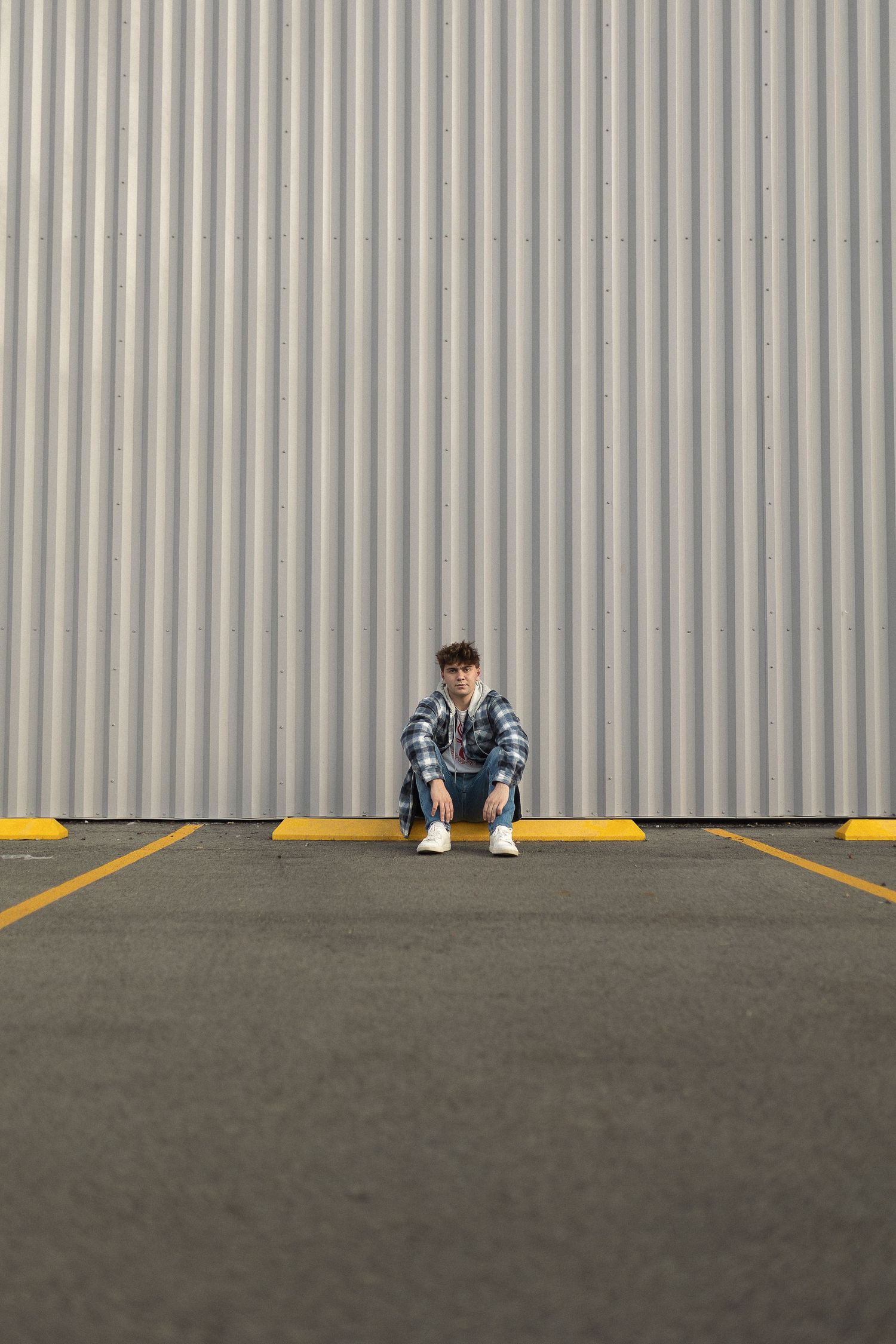 Person in denim sitting against industrial corrugated metal wall with yellow curb.