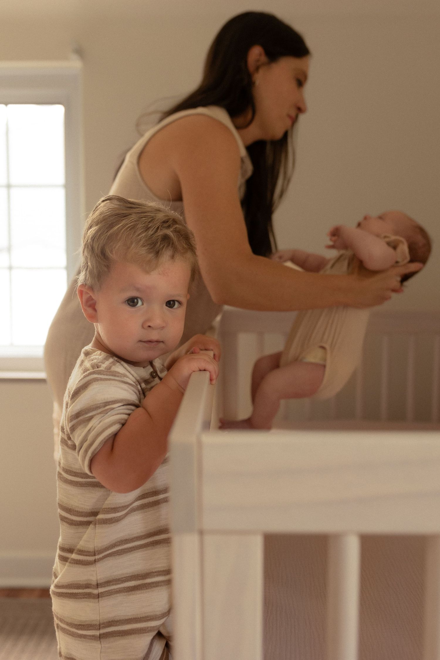A nursery scene with a caregiver tending to a baby while a toddler stands at the changing table.