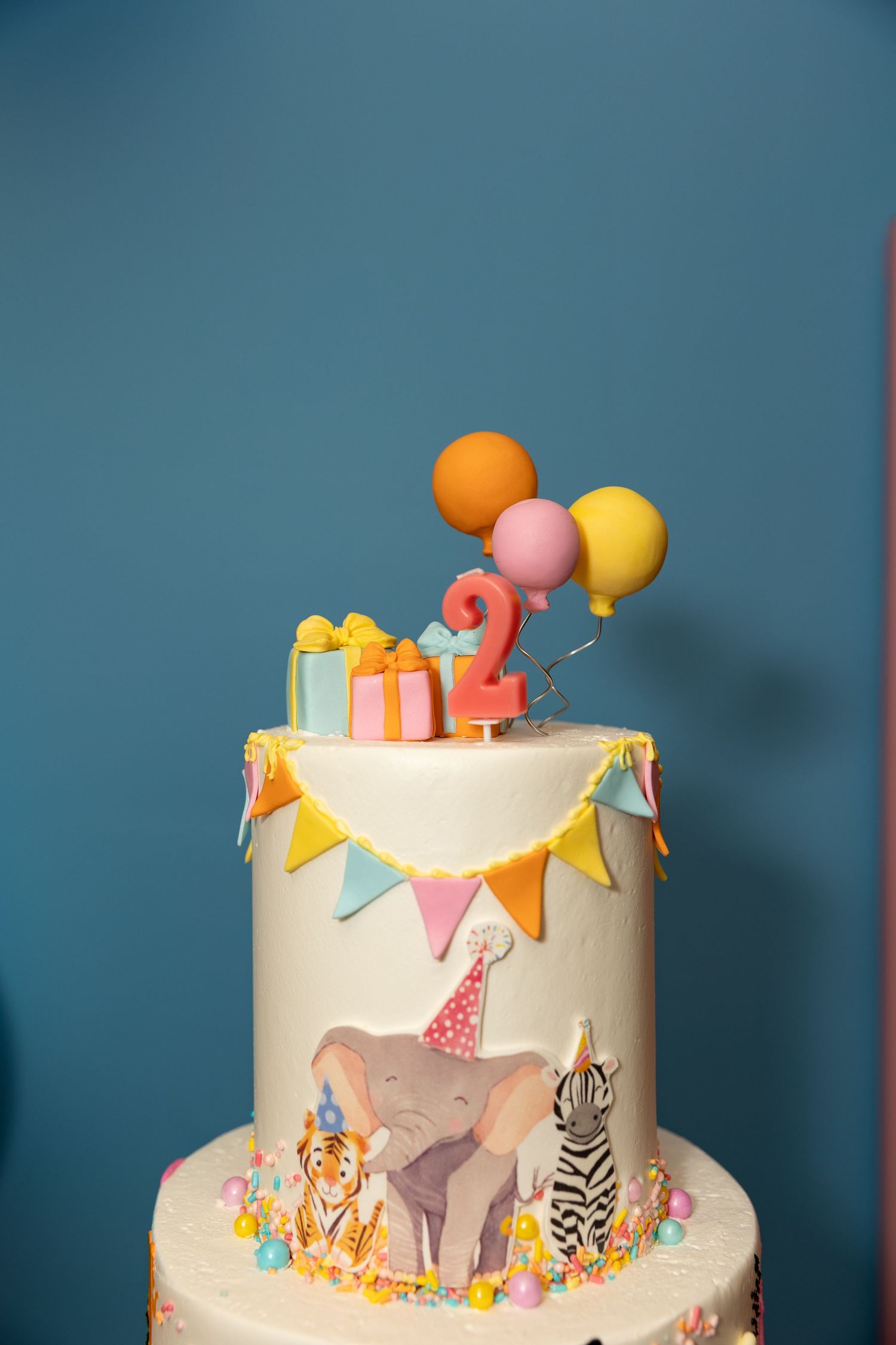 A two-tiered birthday cake decorated with safari animals, balloons and bunting.
