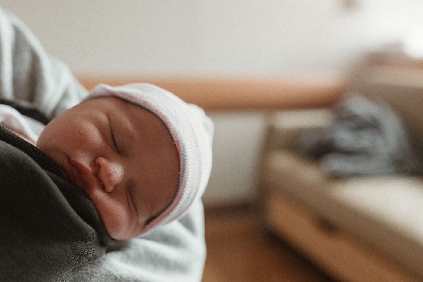 close-up of the tiniest details: sleeping newborn, tiny hat, soft and serene, with cozy in-hospital details blurred gently in the back