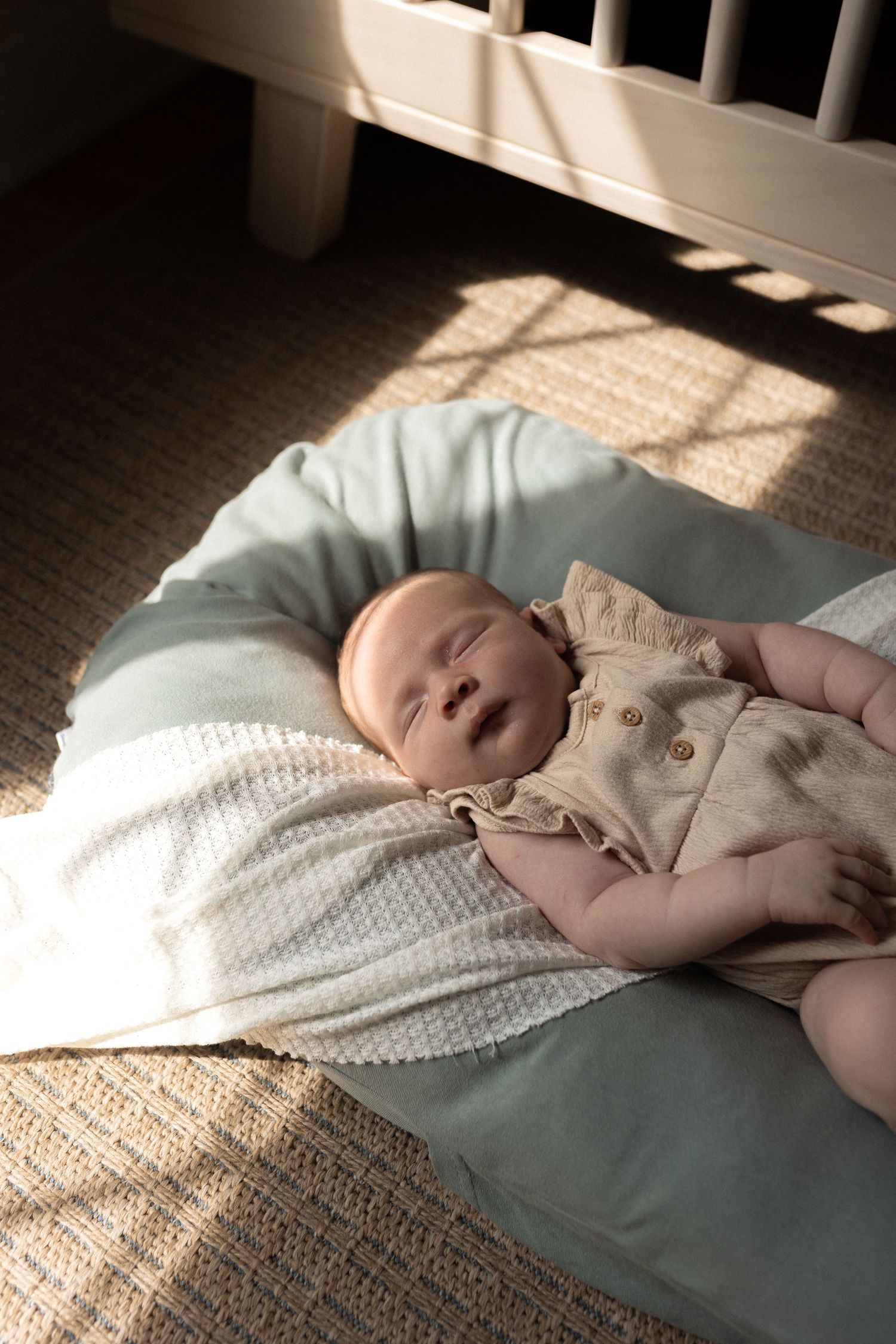 Baby lying on a white blanket in sunlight streaming through window blinds.