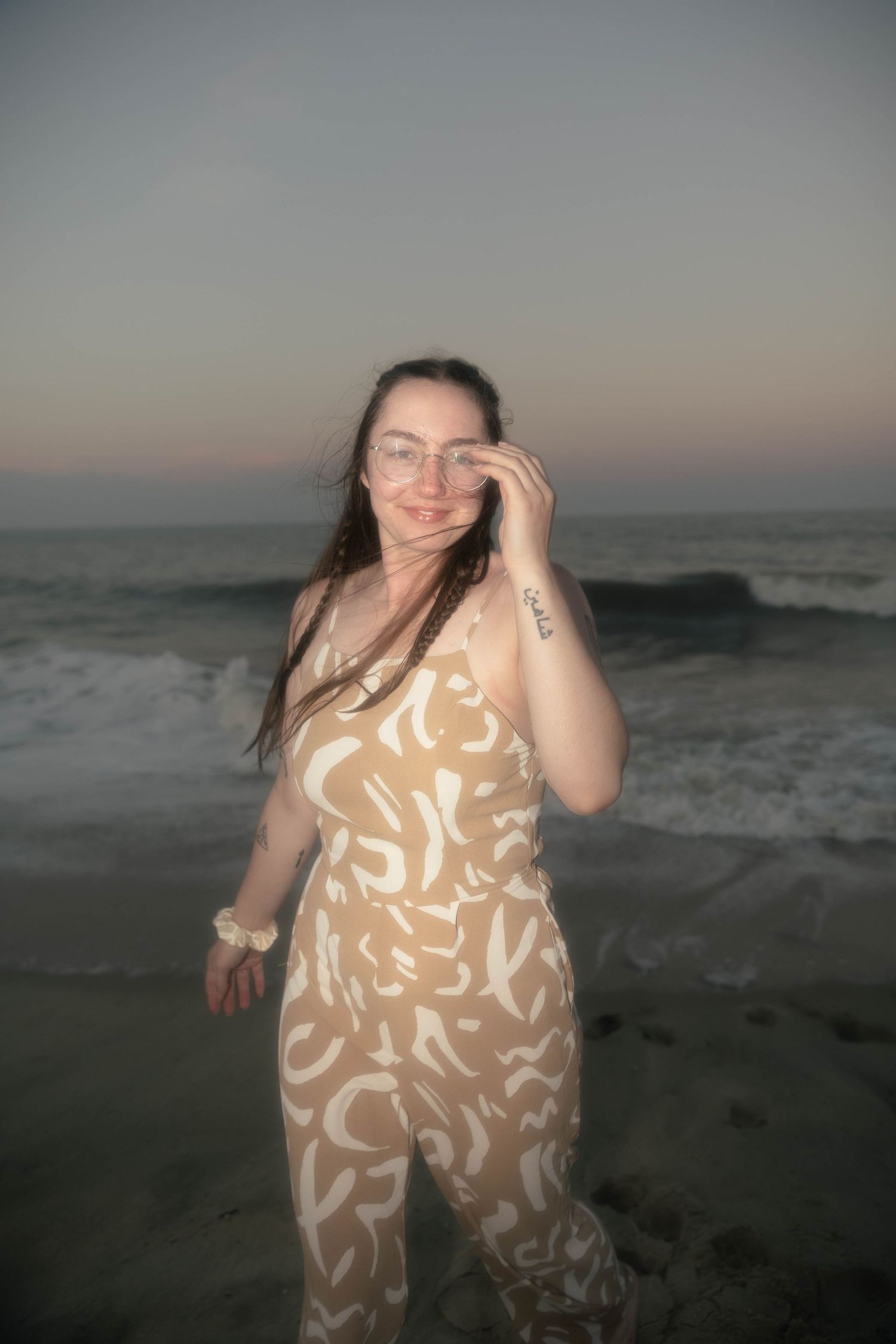 Casual beachwear pose in patterned jumpsuit during sunset by ocean waves.