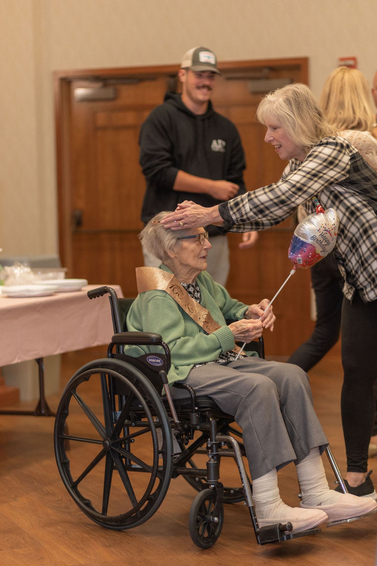 A celebratory gathering with a wheelchair-bound guest receiving well wishes.
