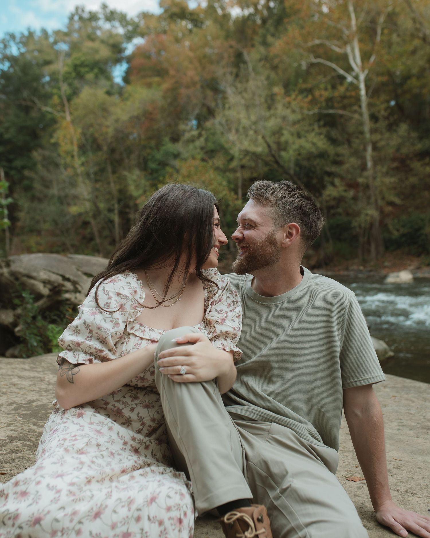 A couple shares an intimate moment together by a river surrounded by autumn trees.