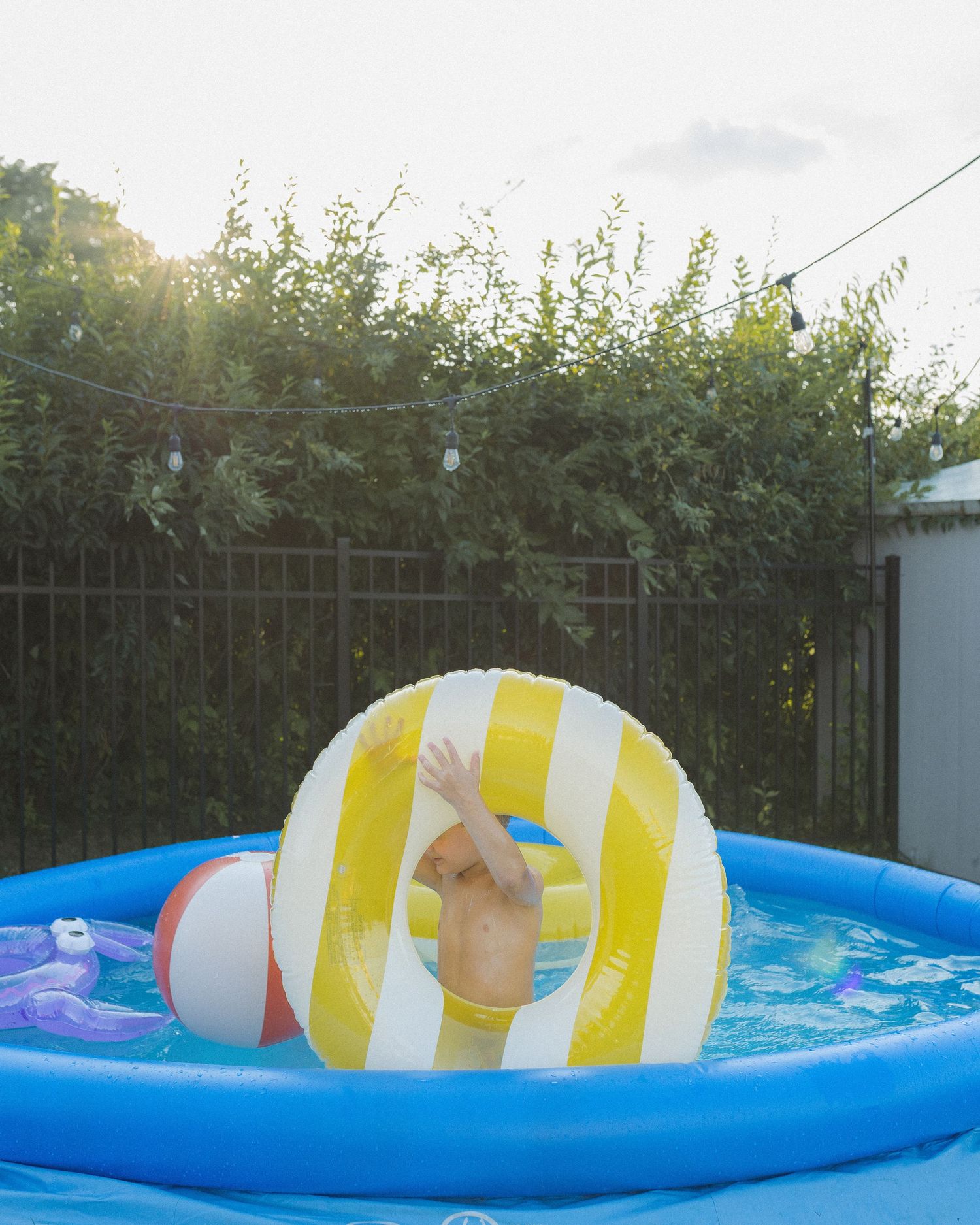 A colorful sequence showing a beach ball floating and sinking in a bright blue inflatable swimming pool over time.