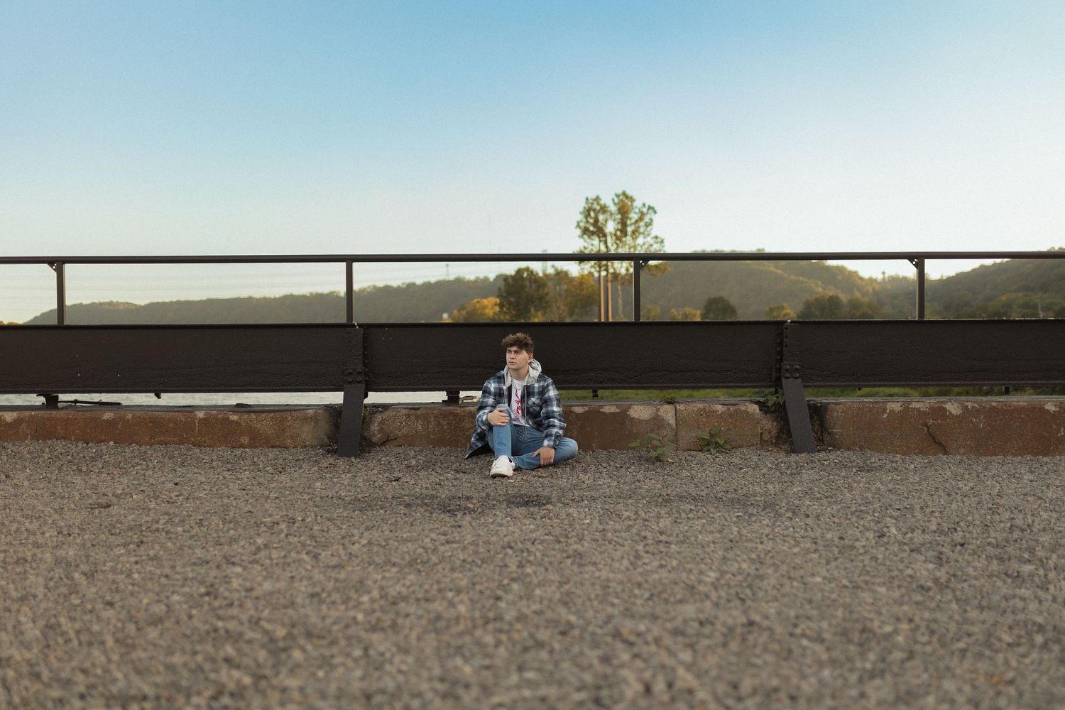 Person sitting against railing with distant scenery in background.