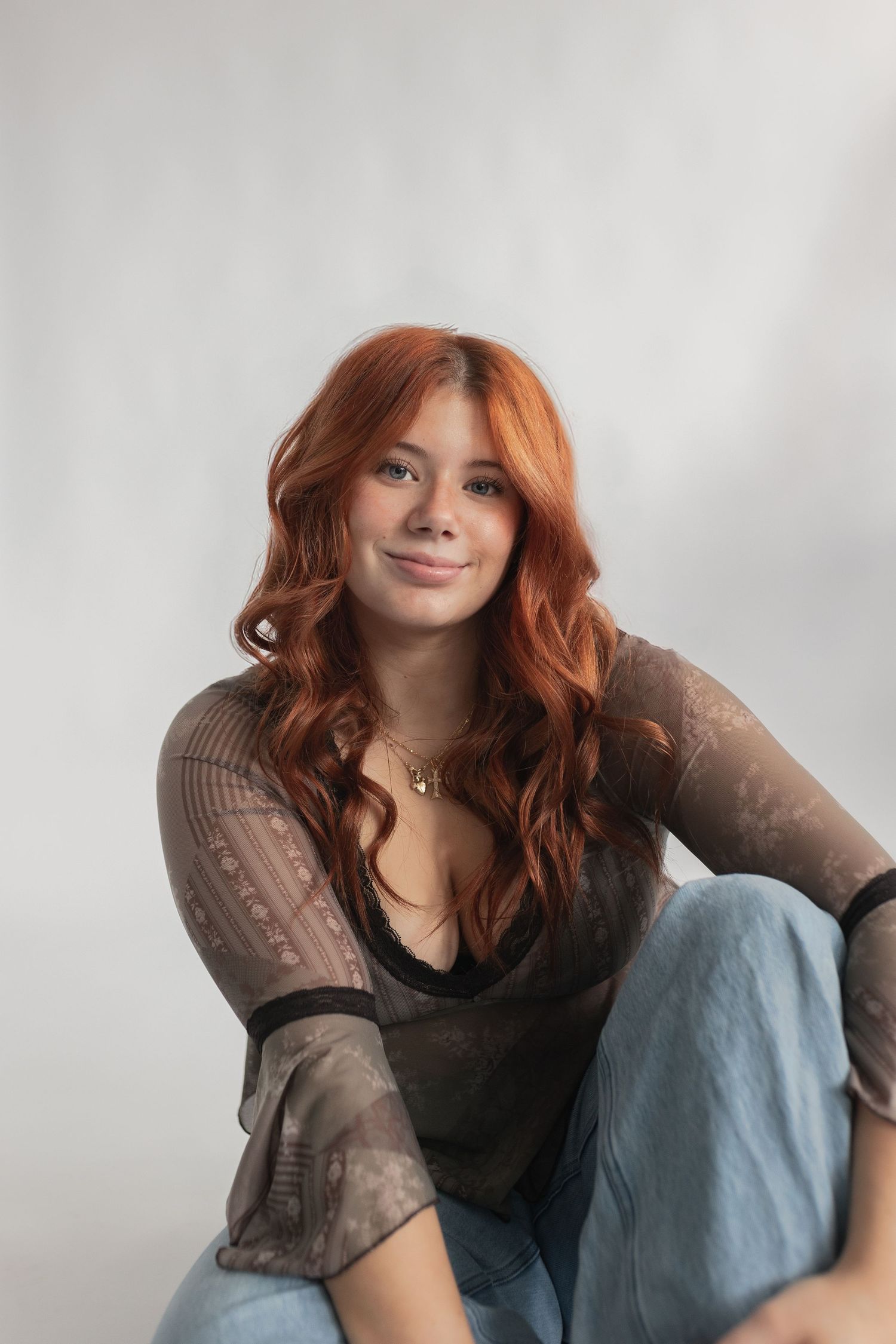 Casual indoor portrait with wavy red hair and dark sheer top.