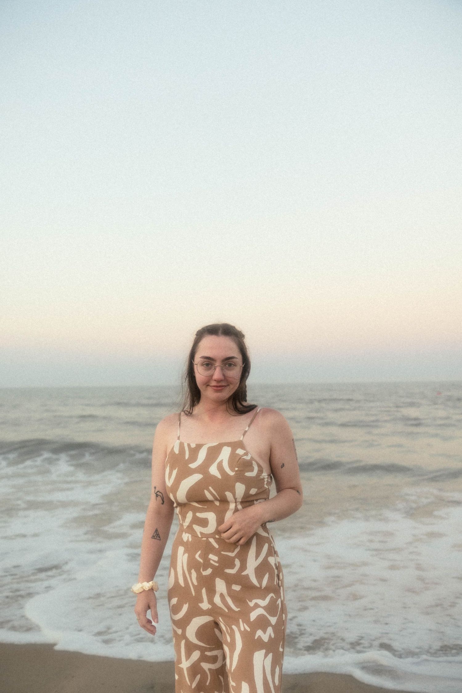 A person stands by ocean waves wearing a tan and white abstract print maxi dress.