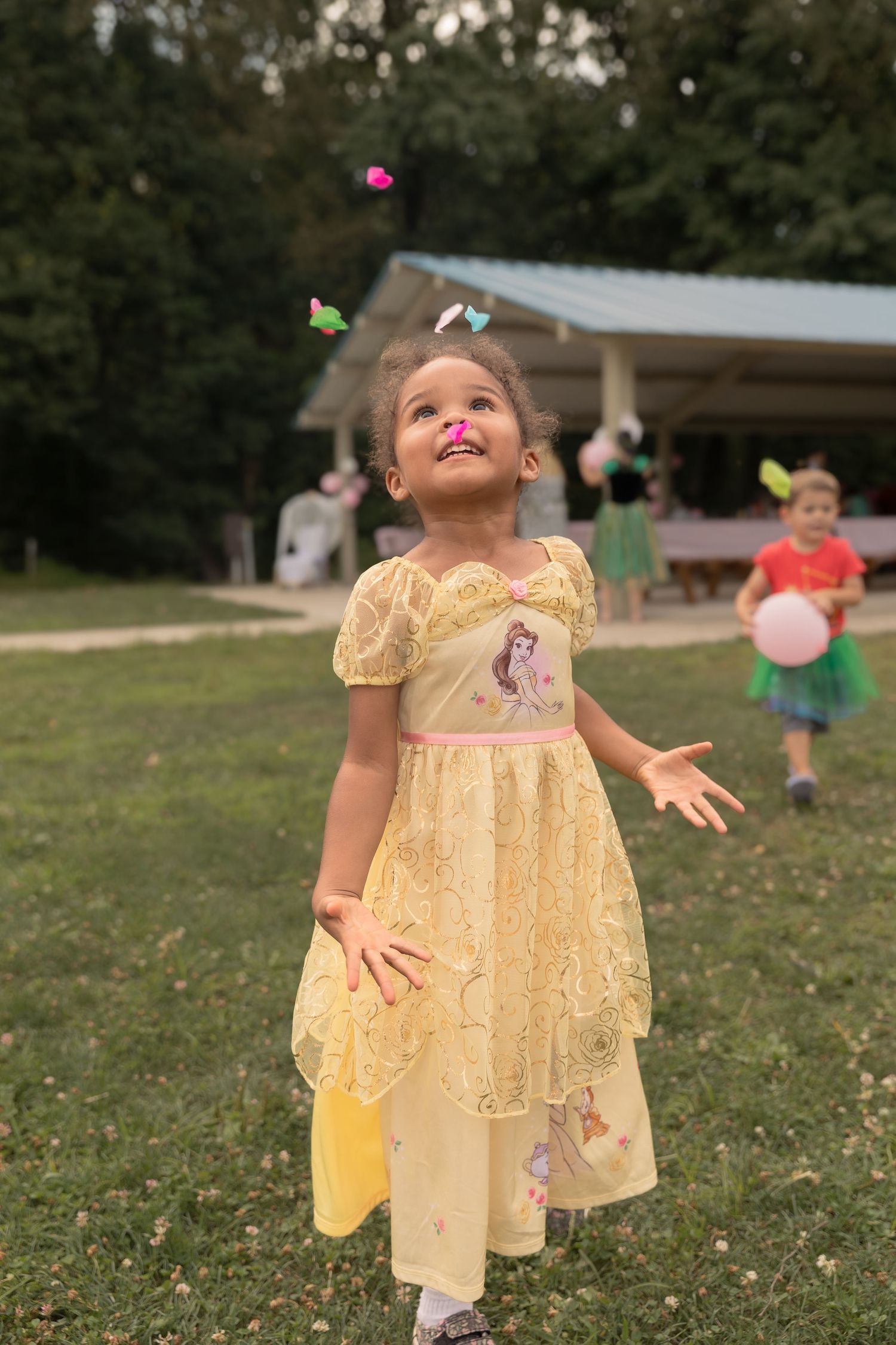 A child in a yellow princess dress looks up with wonder at bubbles floating in the air.