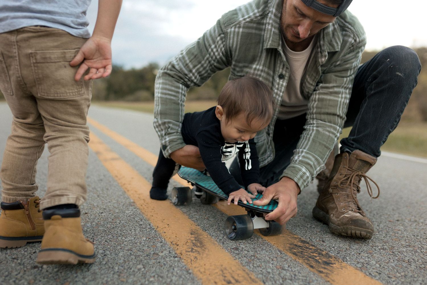 Teaching a child how to skateboard on a road with yellow lines.