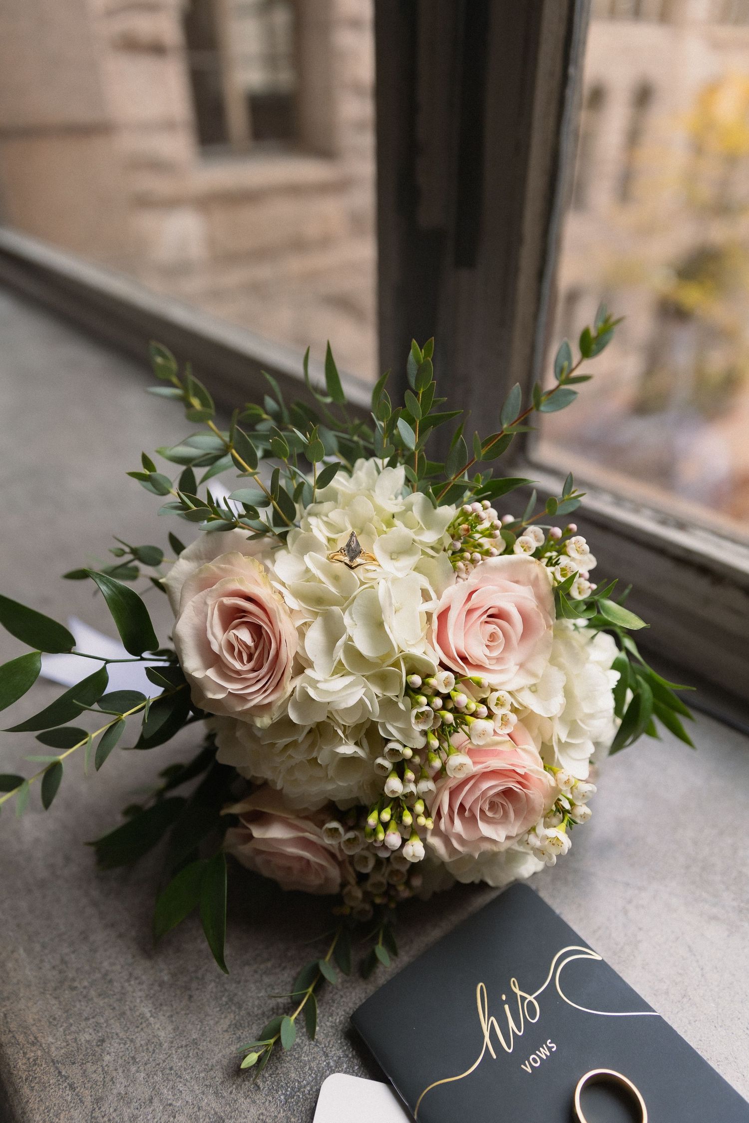 Wedding bouquet with pink roses and white hydrangeas next to a blue book.