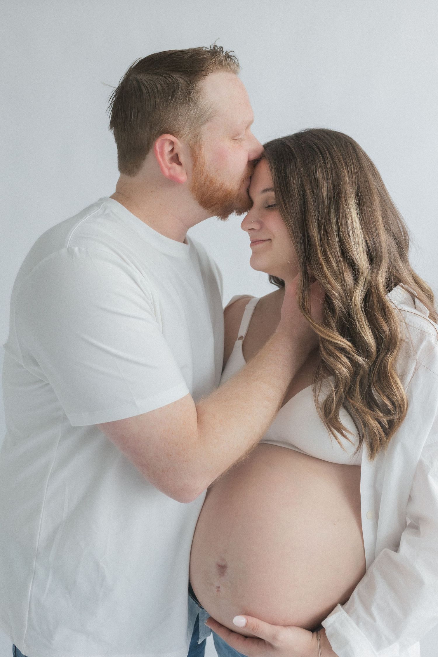 Tender maternity moment captured in soft lighting against white background.