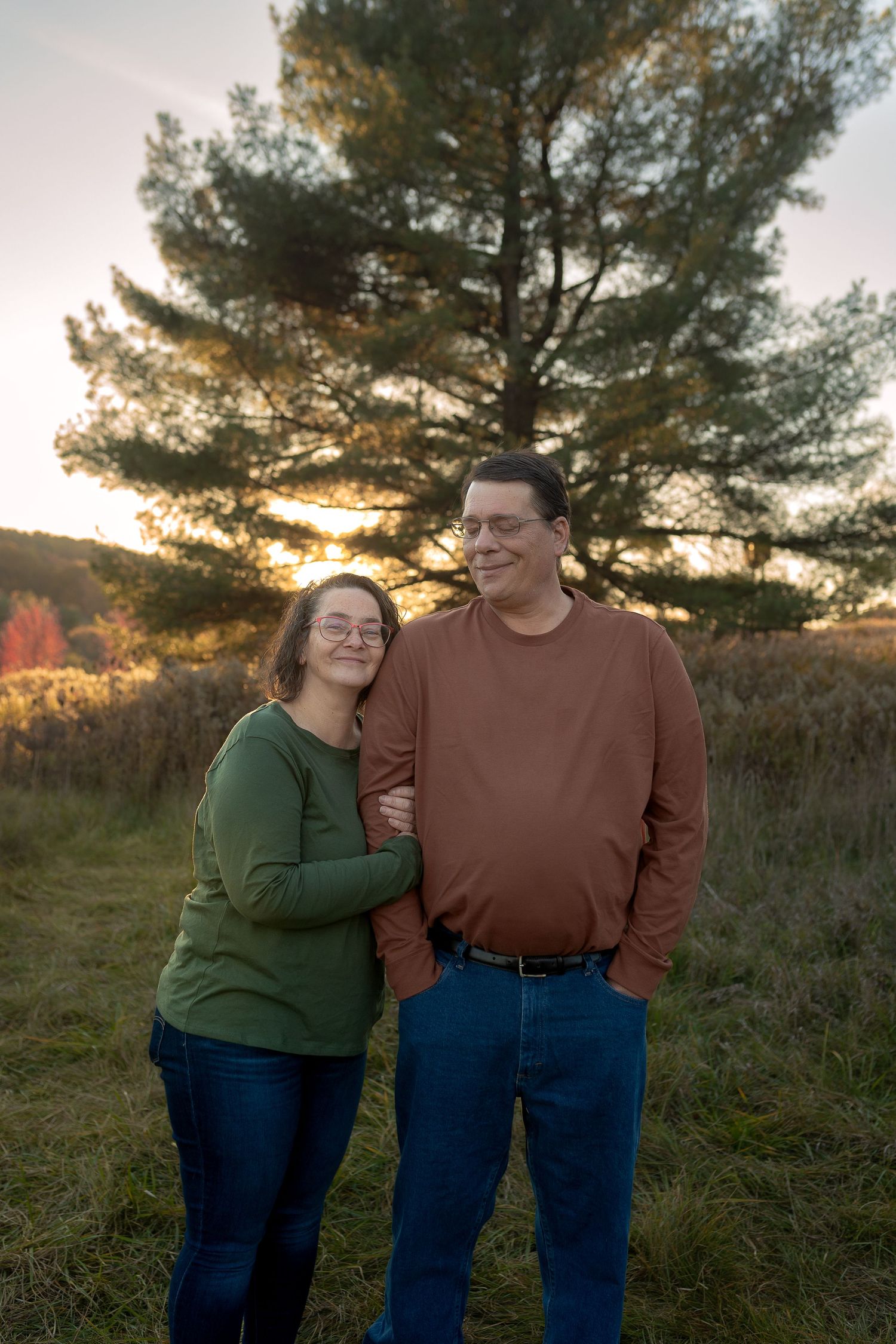 Couple embracing in front of tall pine trees during sunset in a natural setting.