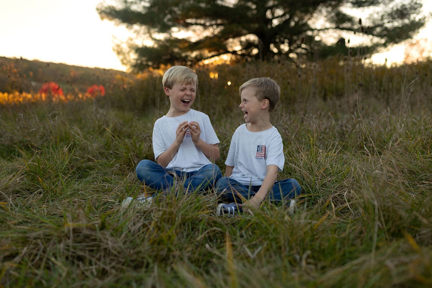 Two young people sitting in grass sharing a joyful moment at sunset.