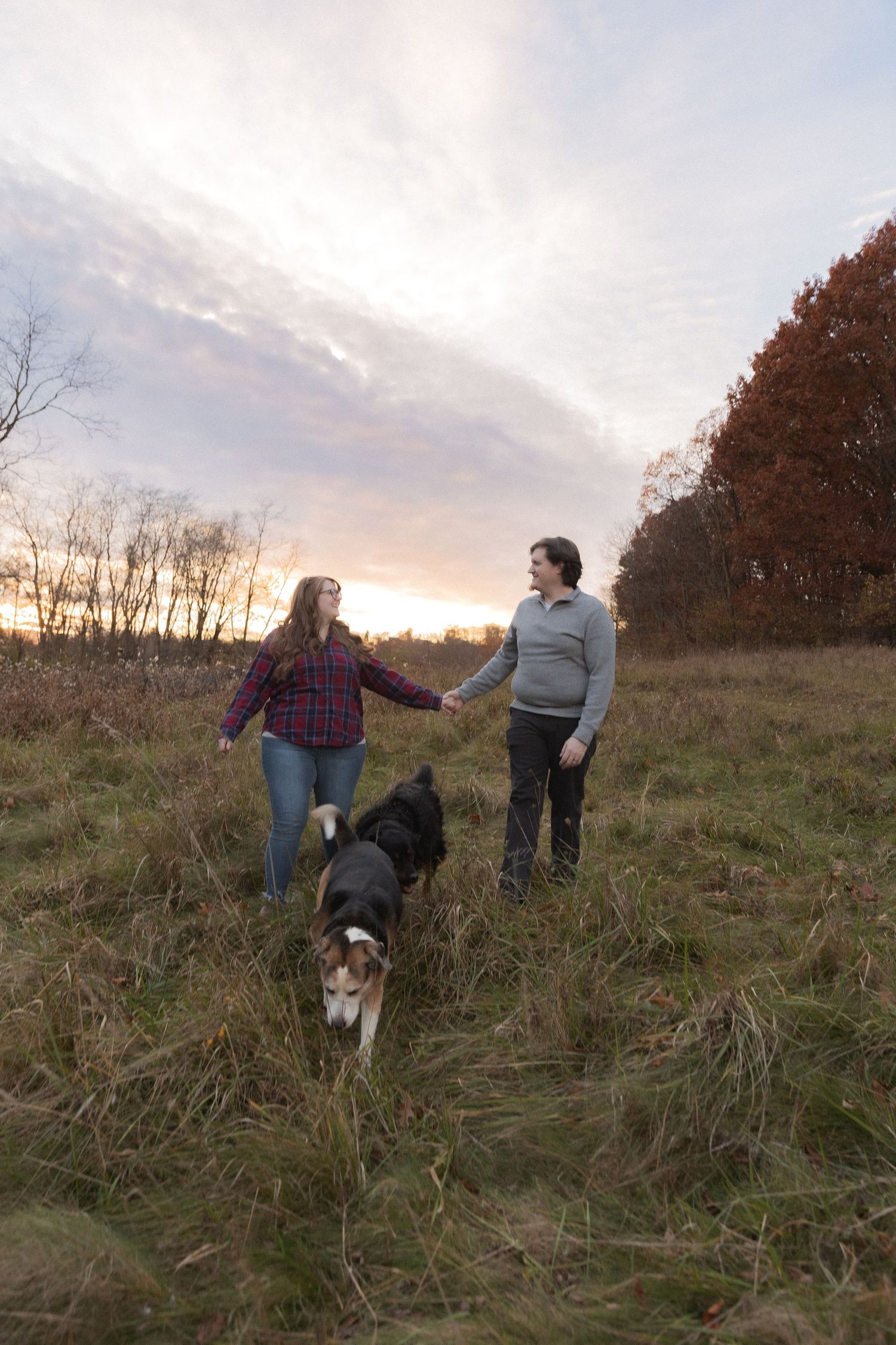 Two people walking with their dog on a grassy hill during sunset.