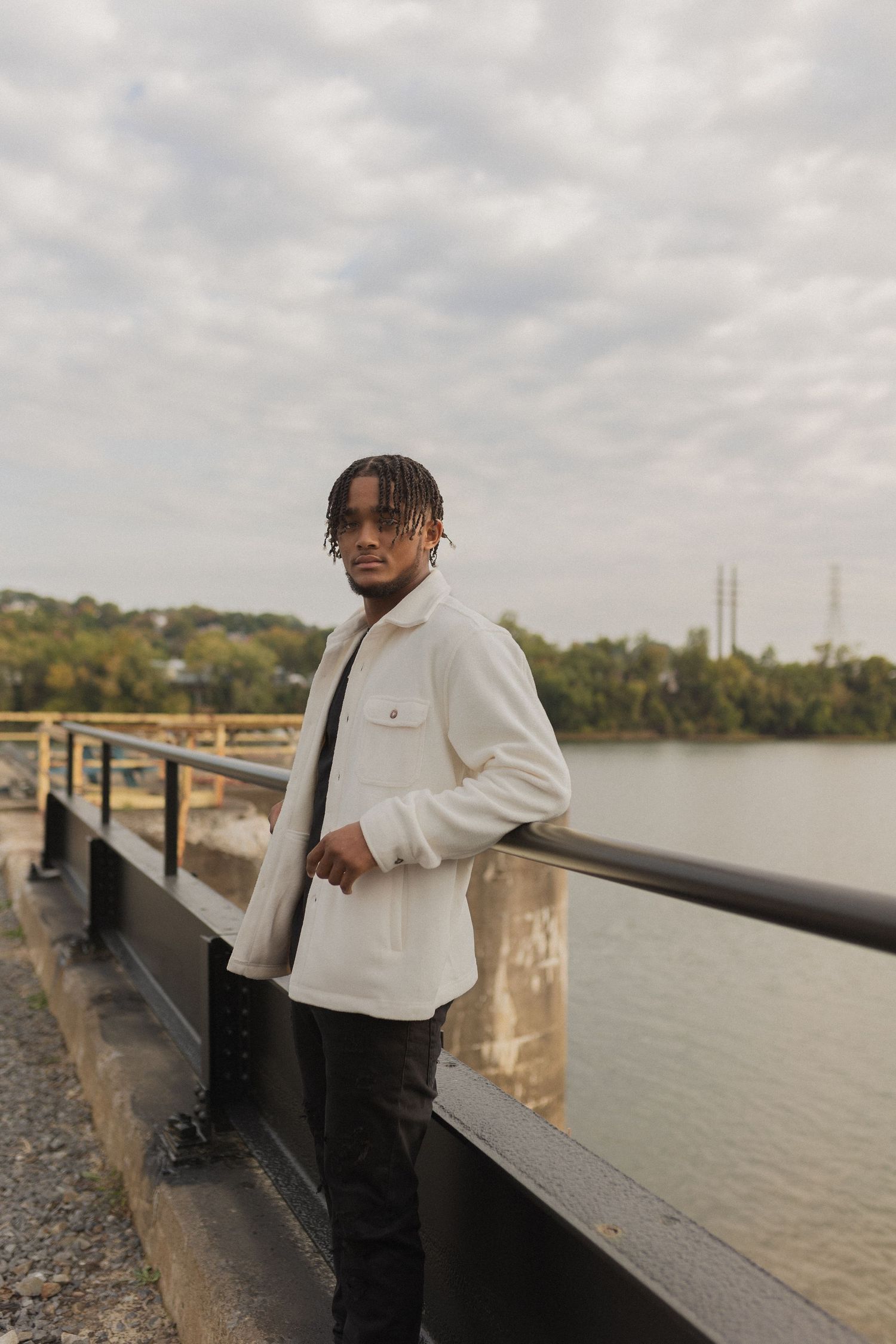 Portrait at waterfront wearing white jacket against cloudy sky.