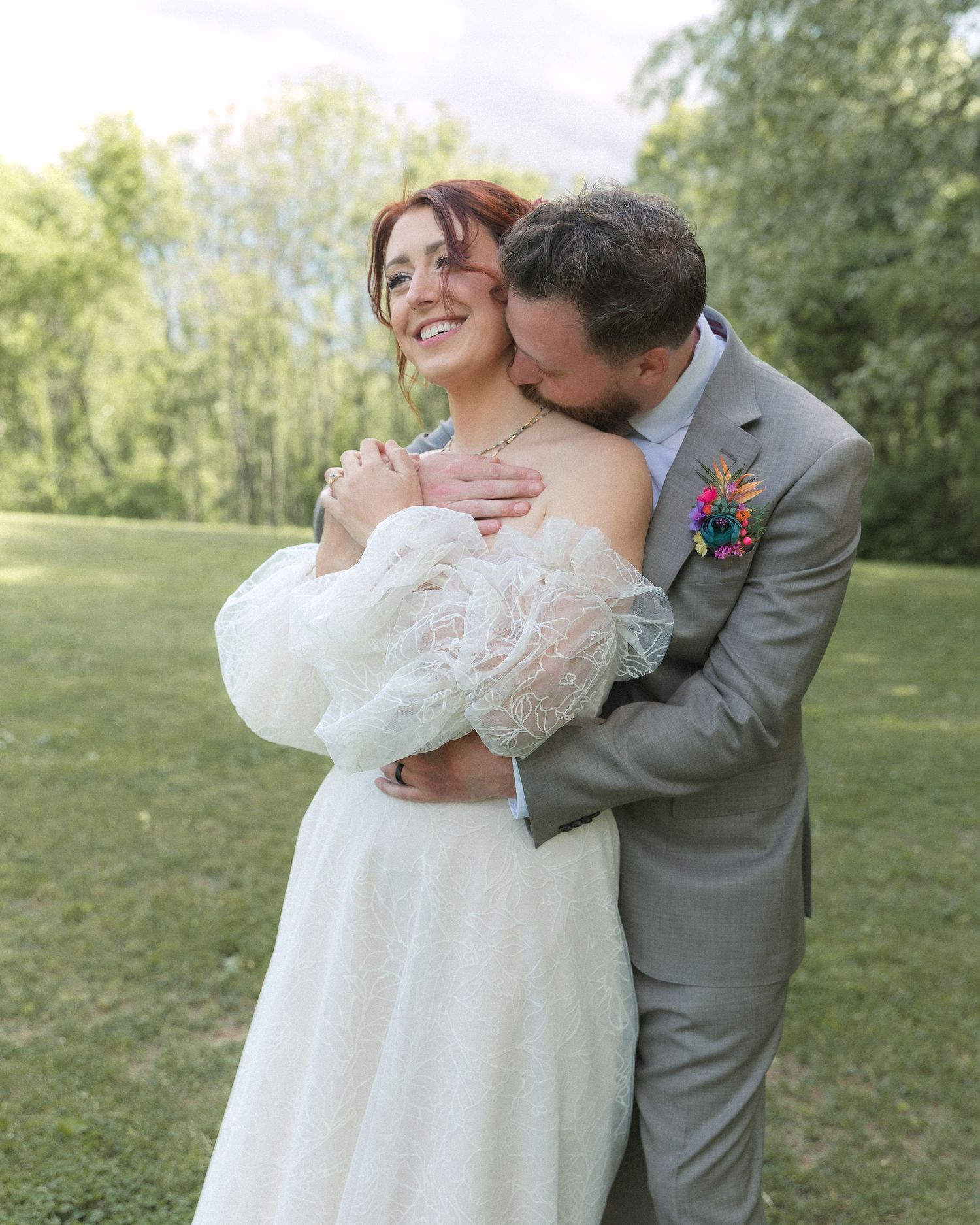 A romantic outdoor wedding moment captured in a lush green garden setting with a couple in traditional white dress and grey suit.