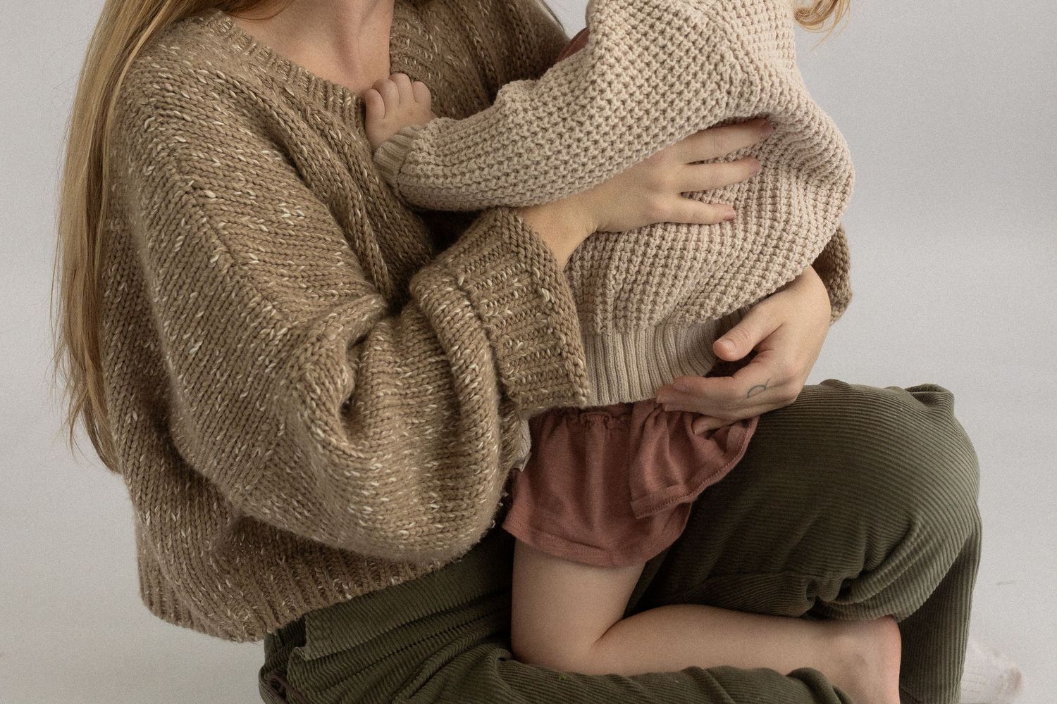 Close-up of gentle embrace wearing warm knit sweater against minimalist background.