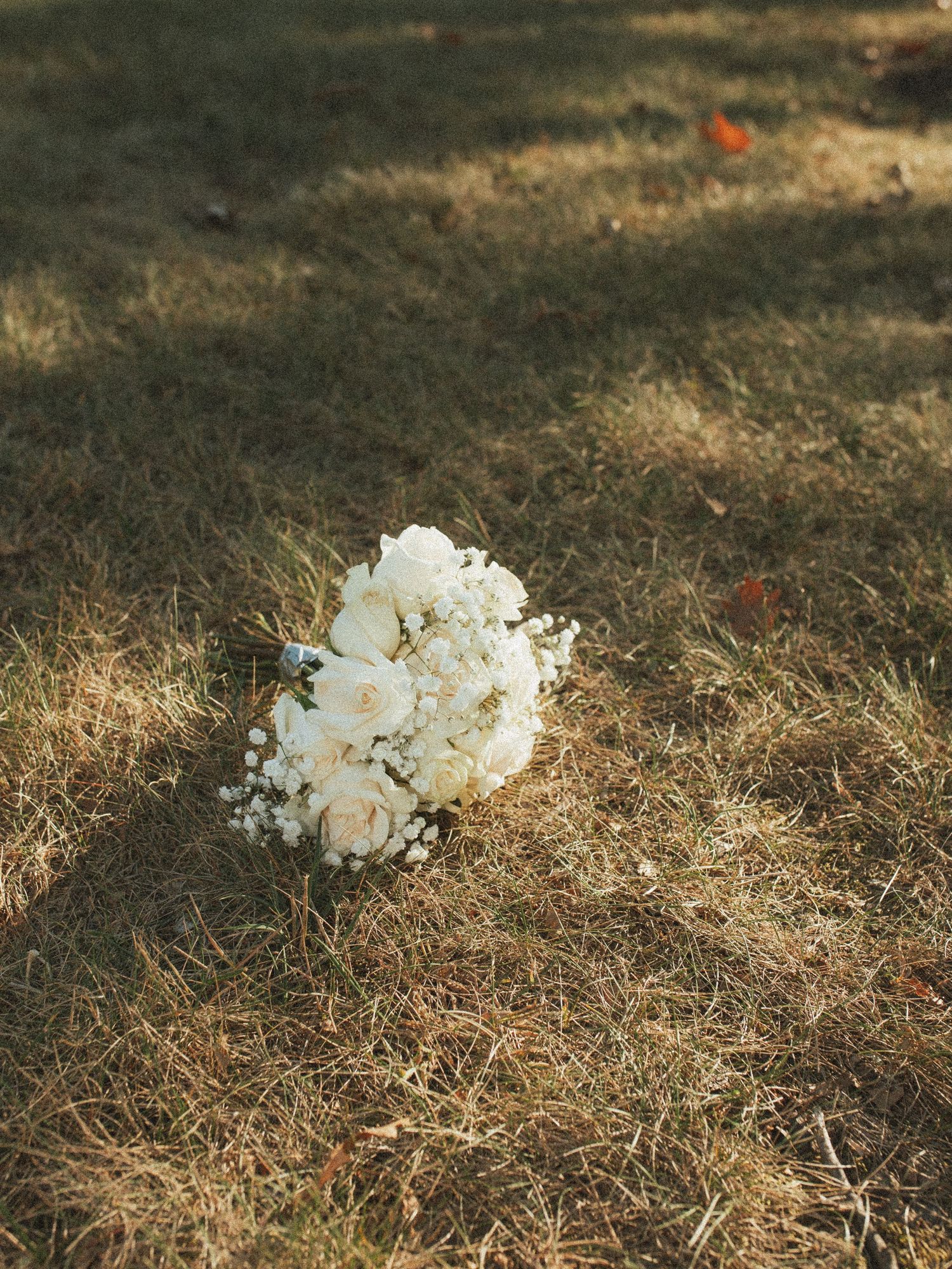 A delicate white floral bouquet rests on dried brown grass in natural outdoor lighting.