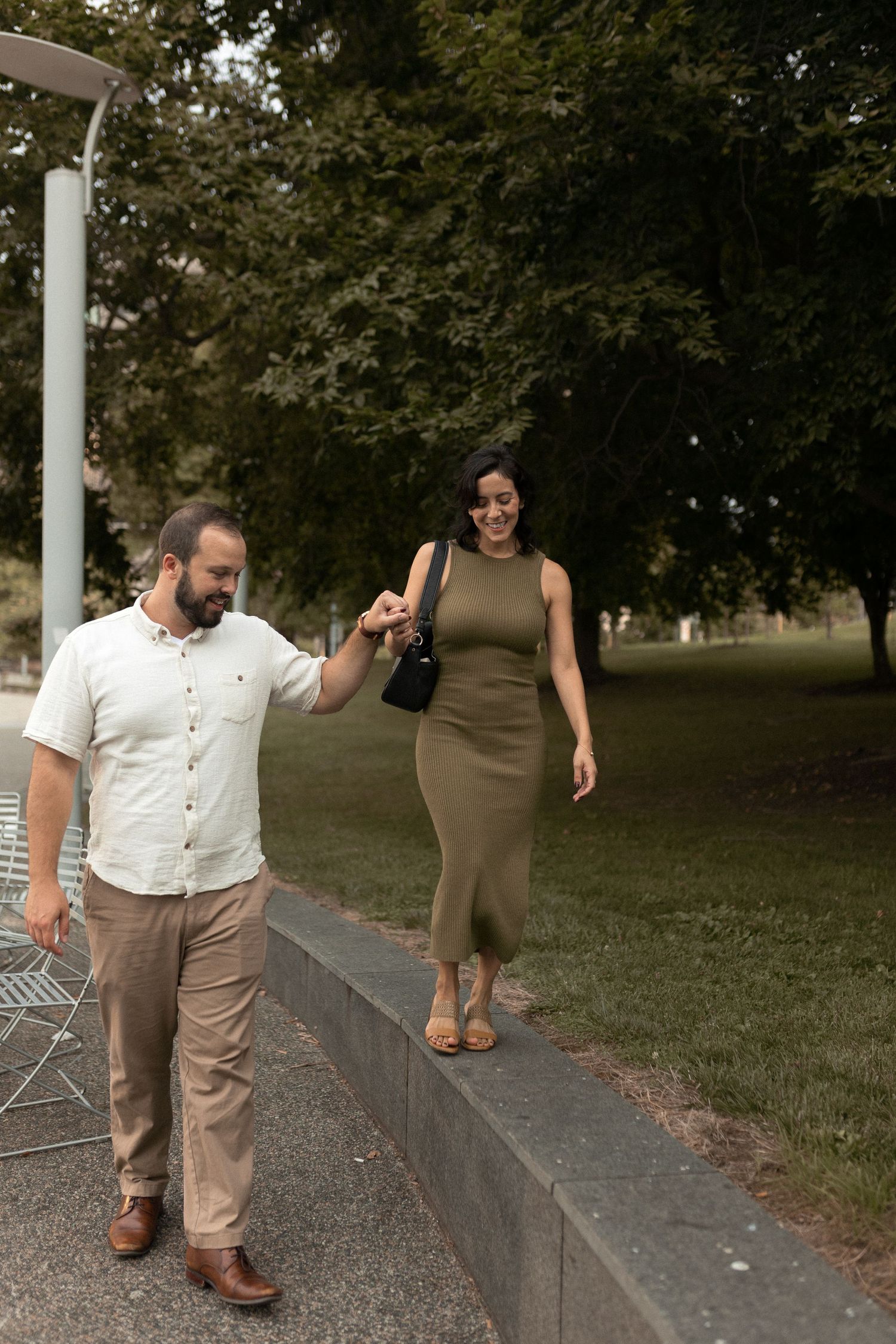Engaged couple walking hand-in-hand through the park, romantic storytelling photo with film-inspired softness.