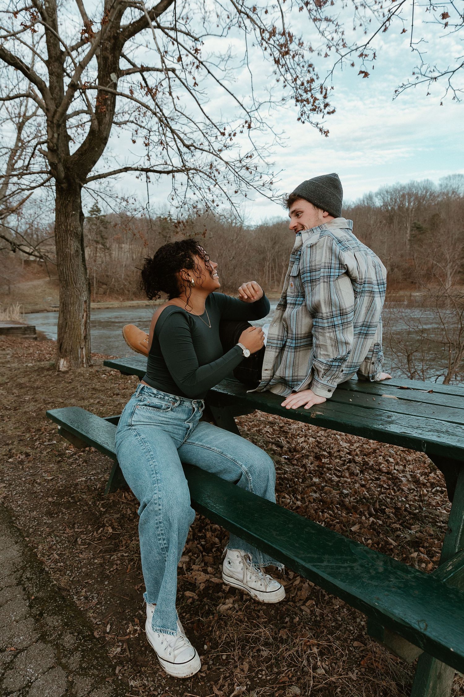 Couple laughing and leaning in at a green picnic bench, warm film look and candid storytelling chemistry.