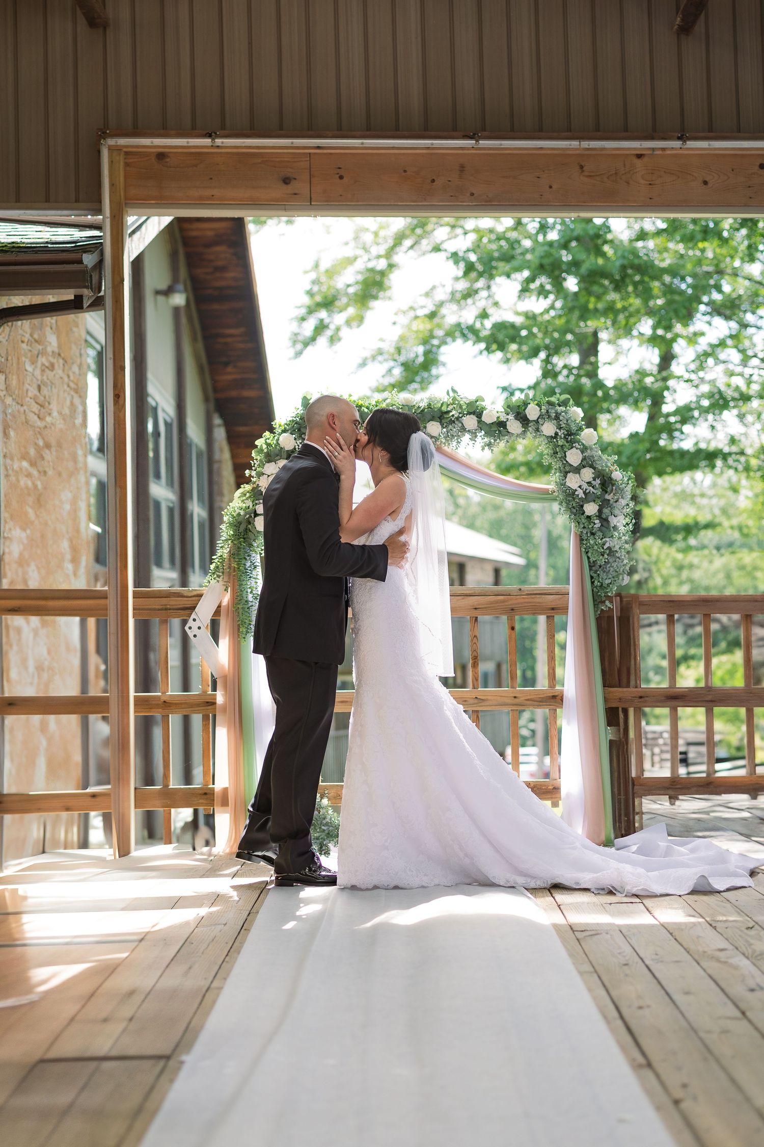 A bride and groom dance intimately on a rustic wooden deck surrounded by lush greenery at a rustic venue.
