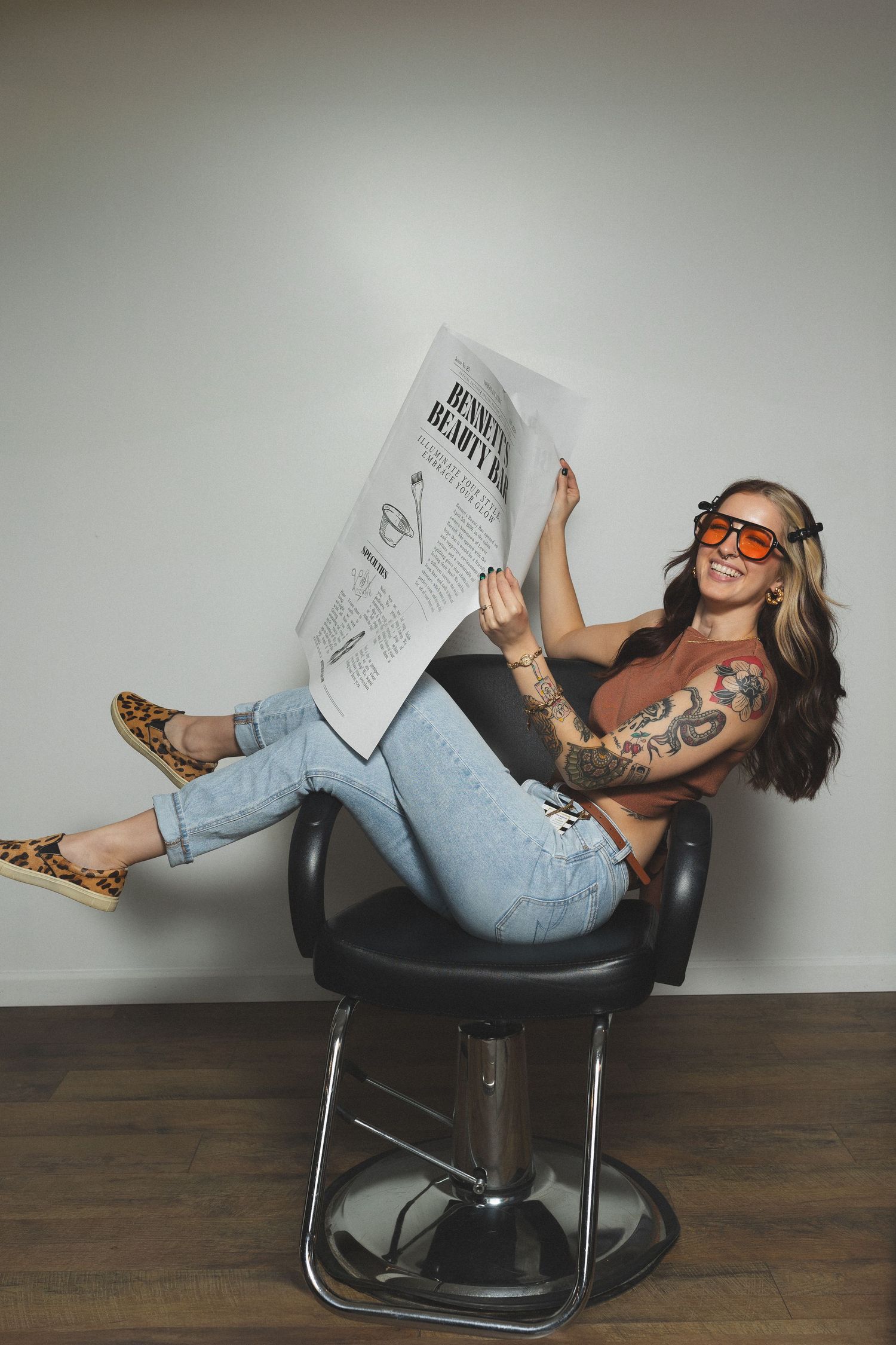 Woman in casual wear lounging in a salon chair while reading a newspaper.