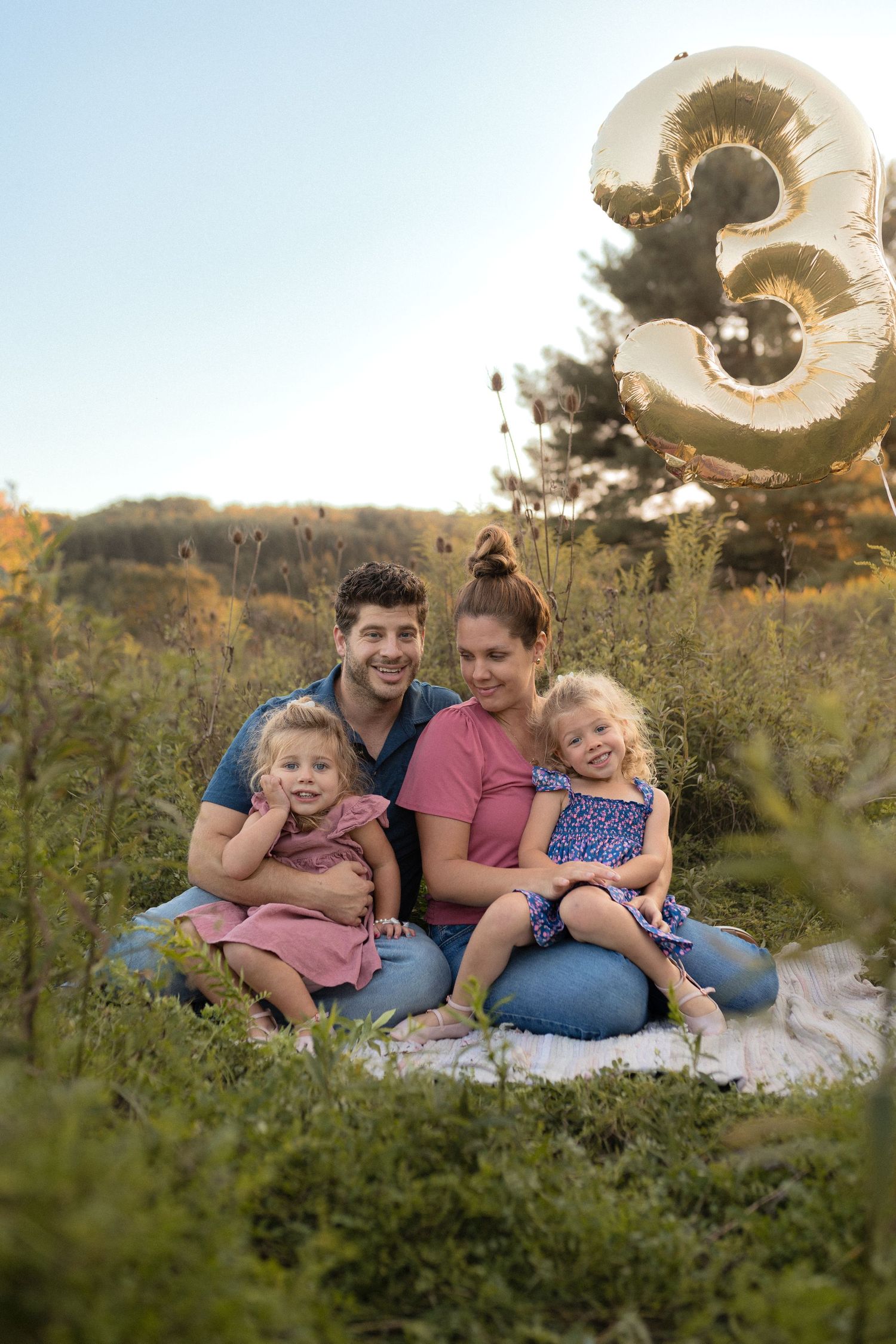 Family celebrates with number 3 balloon during outdoor photo session.