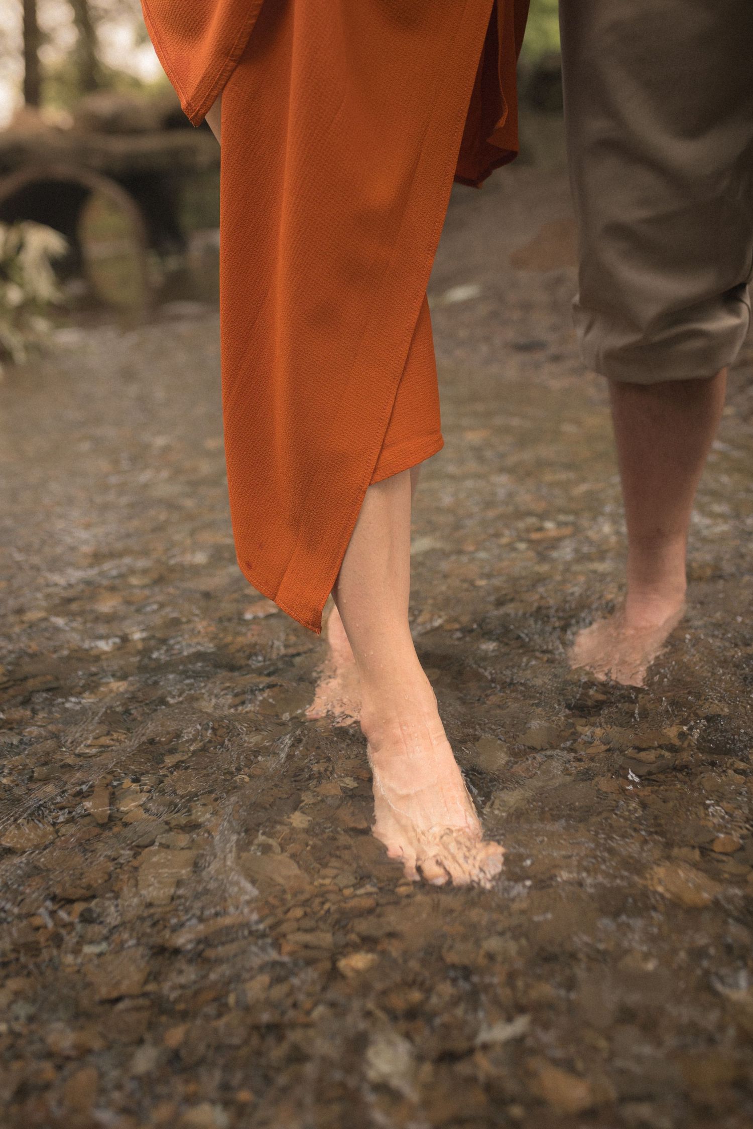 Barefoot lovers walking through a creek, detail shot with warm film tones and poetic storytelling energy.