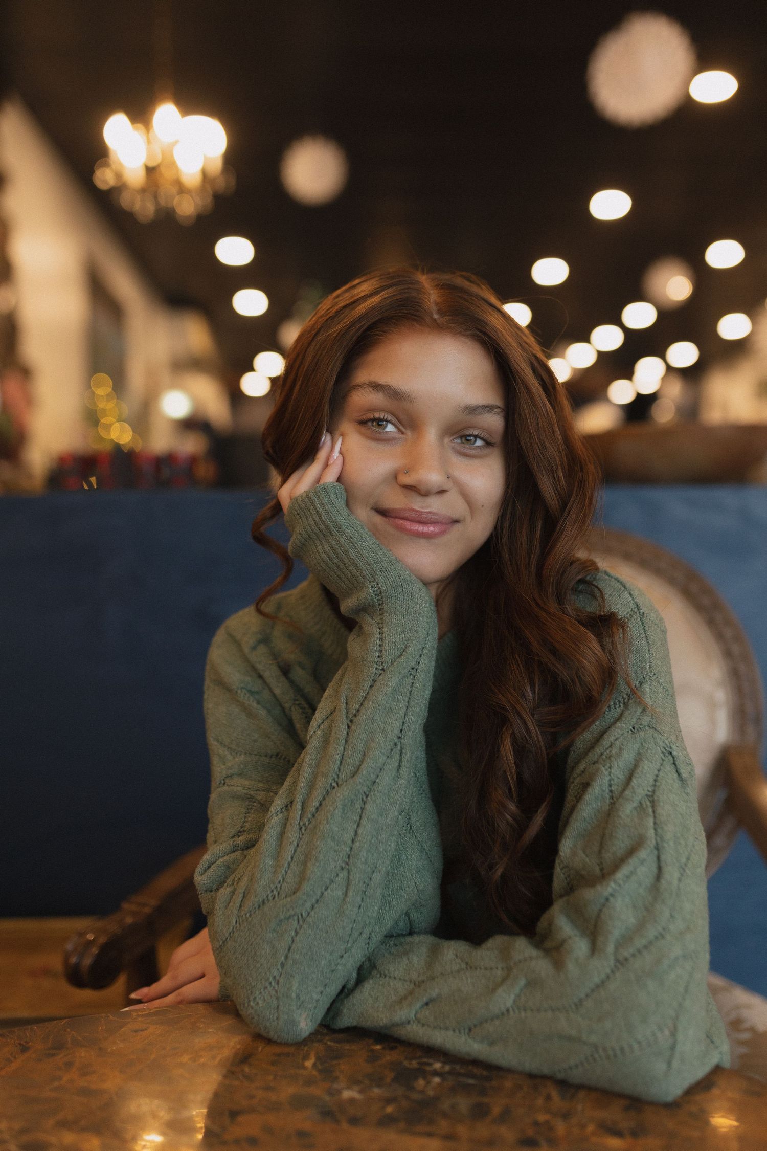 Person in mint green sweater relaxes on blue couch with warm lighting and bokeh background.