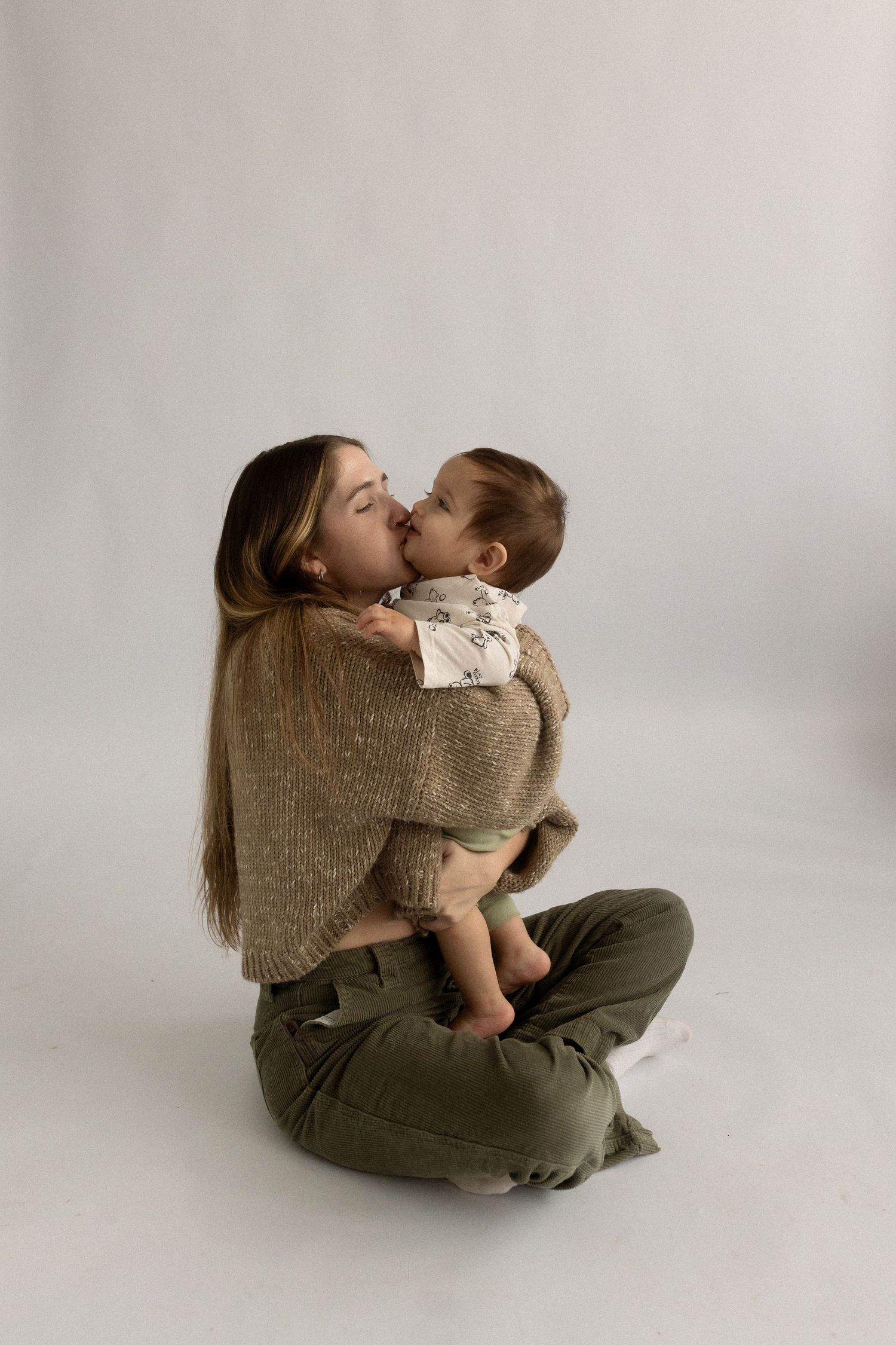 Parent and child sharing affectionate moment in studio setting wearing neutral toned clothing.