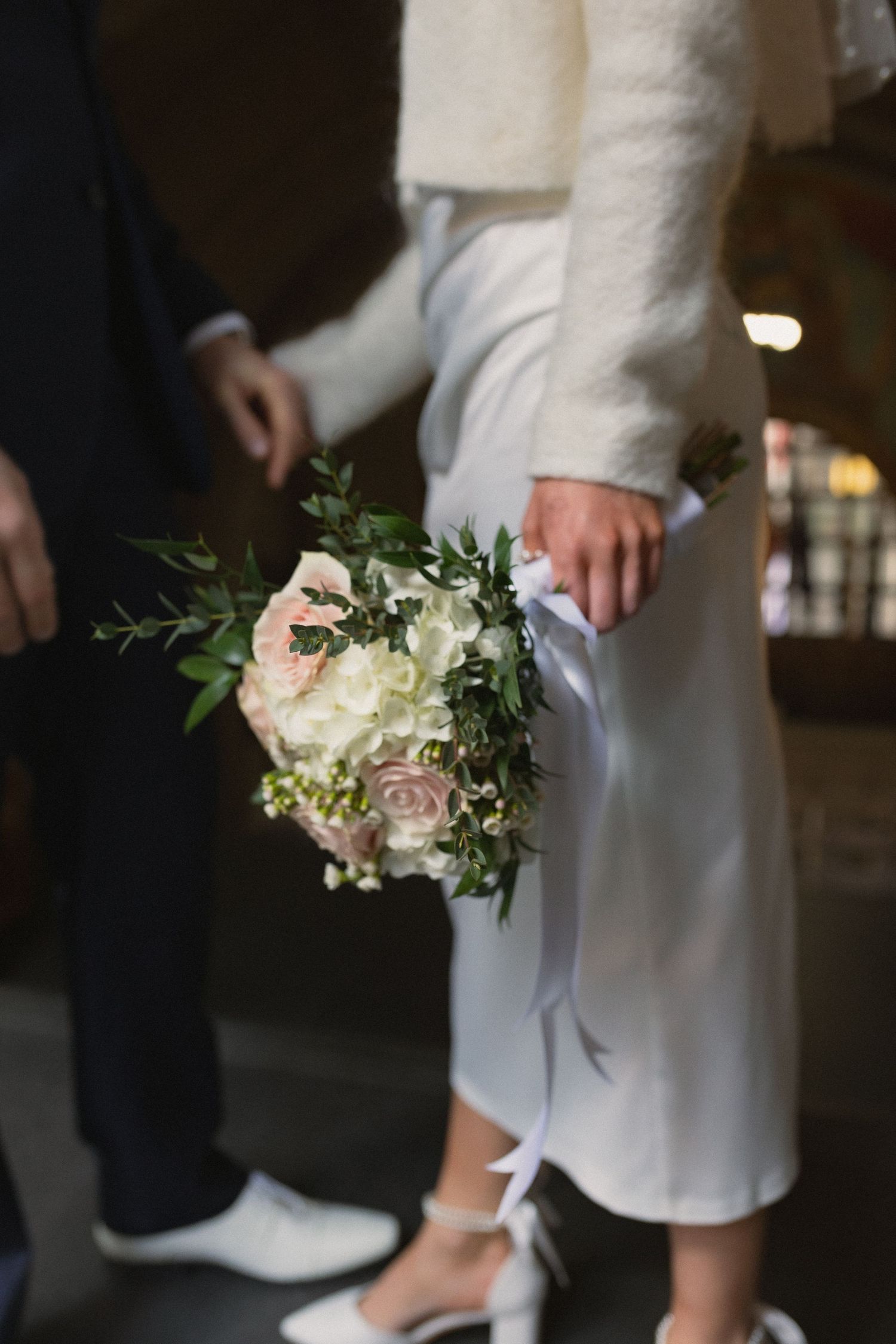 Close-up of wedding bouquet with white and pink flowers held against white dress.