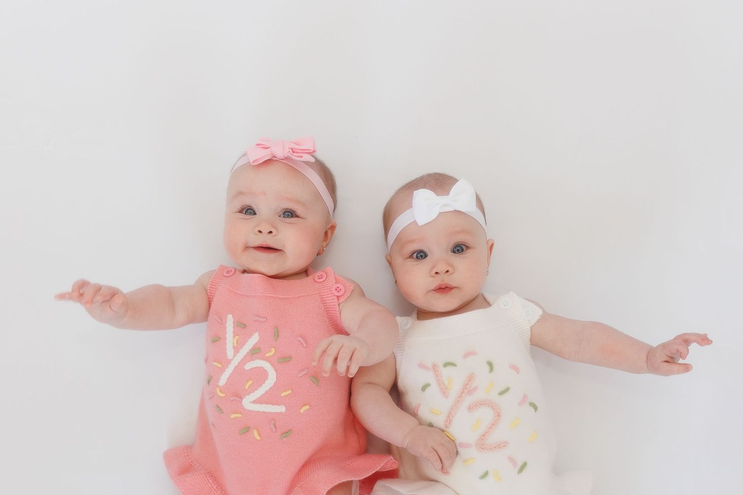 Studio milestone photo of 6-month-old twins in soft whites and pinks, light and airy edit with storytelling charm.