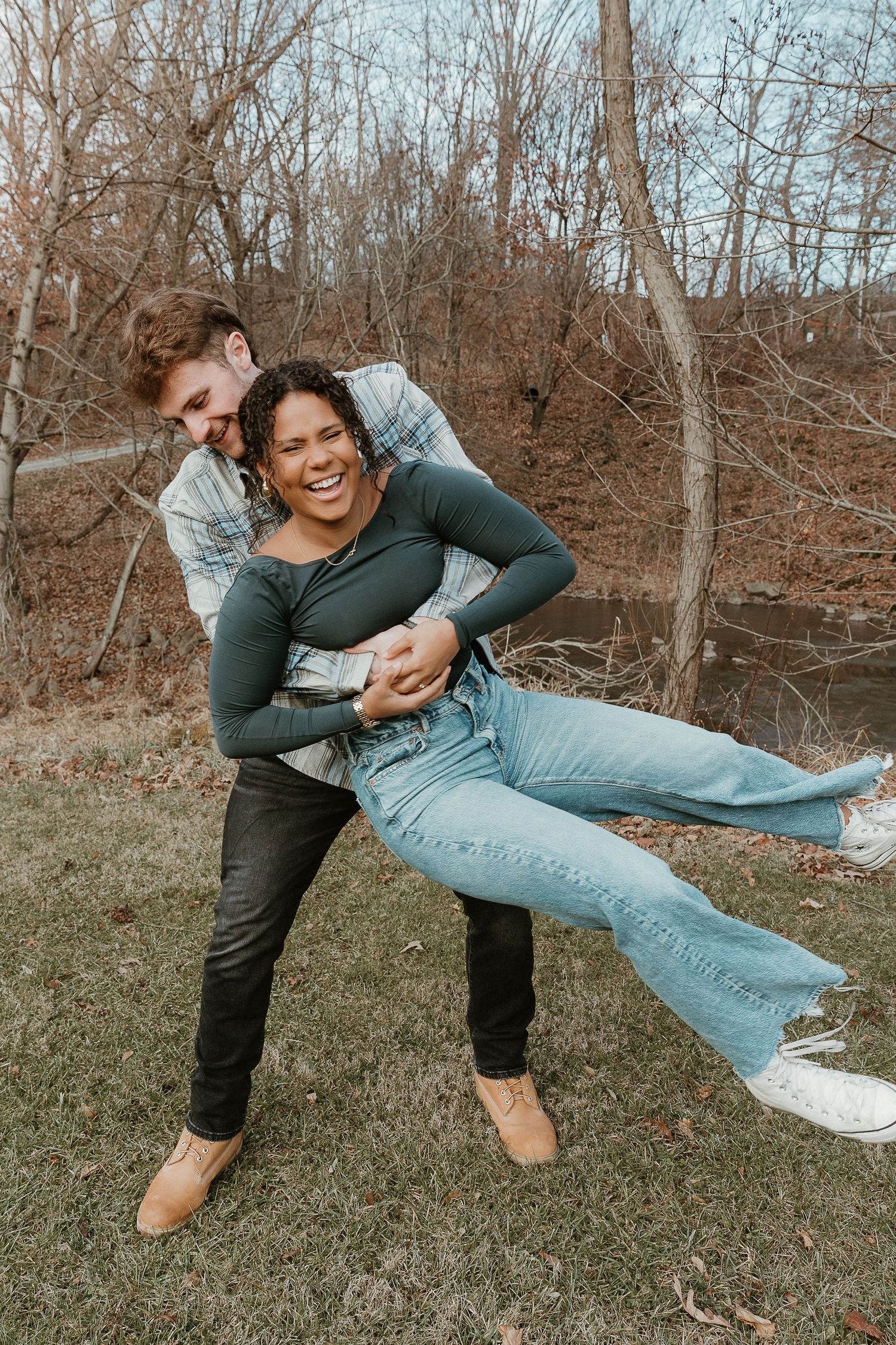 Playful couple moment as he spins her around in a field, candid lifestyle photography with warm film-inspired energy.