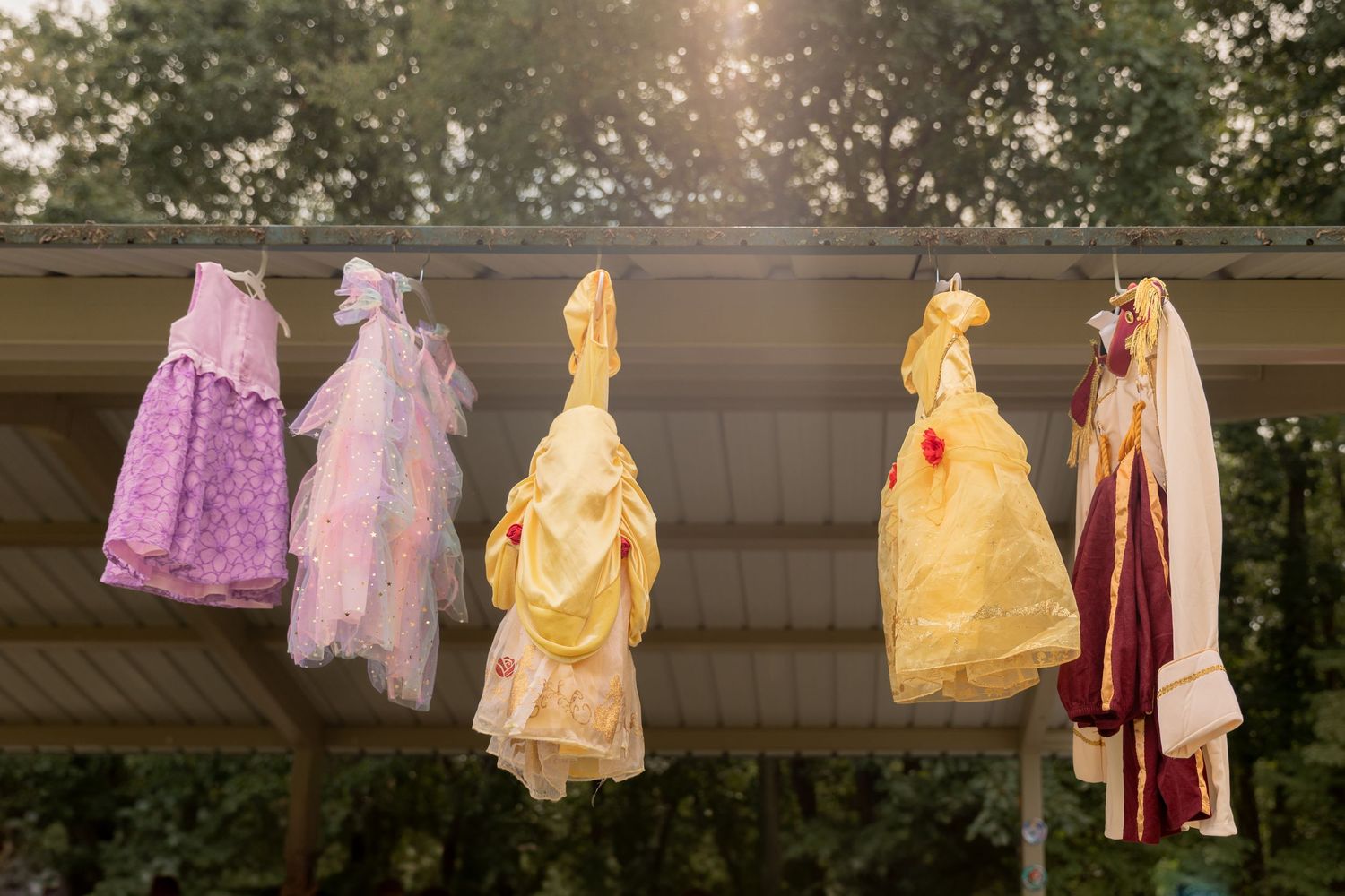Colorful princess dresses hanging on display at sunset including pink, yellow and burgundy gowns.