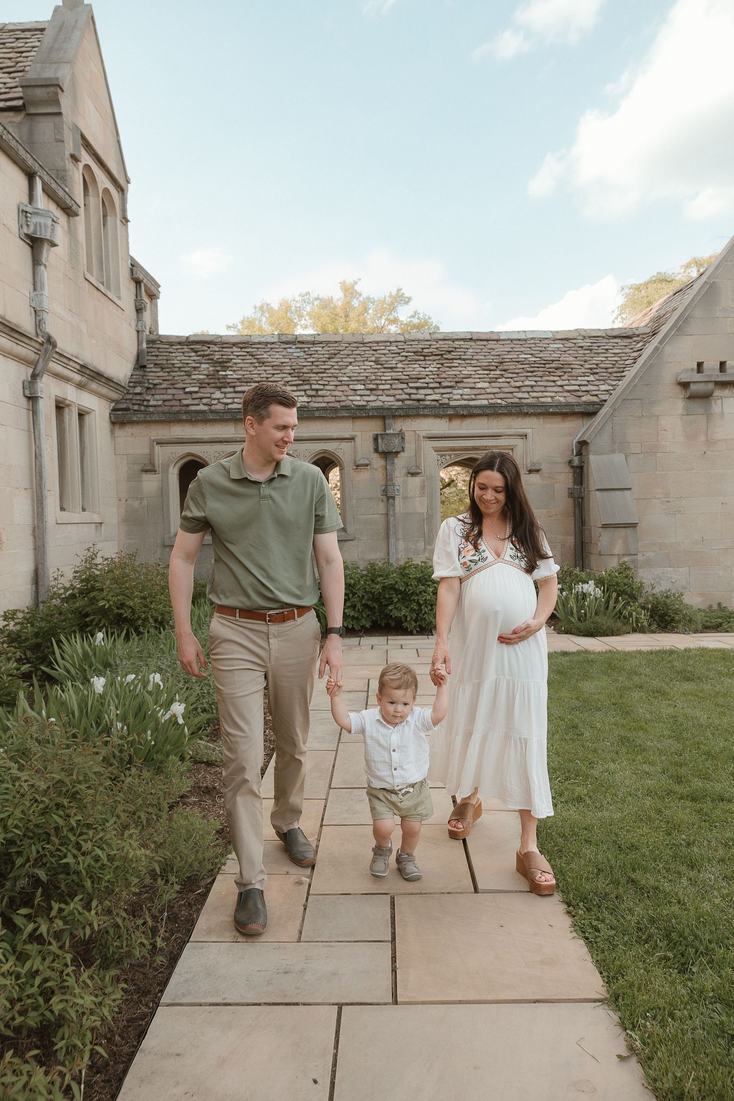 Film-style storytelling photo of a growing family walking hand-in-hand at a timeless stone estate, soft golden light.