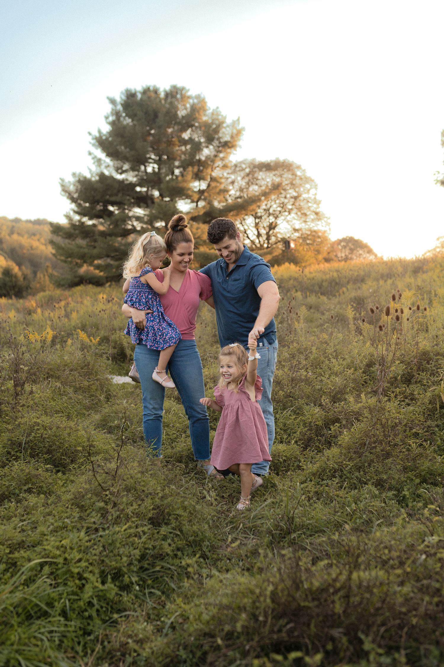 Family enjoys playful moment together on grassy hillside during sunset.