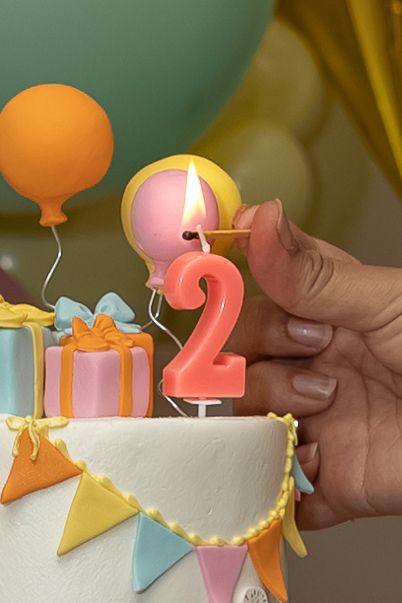 Hand lighting a number 2 candle on a white birthday cake with colorful bunting.