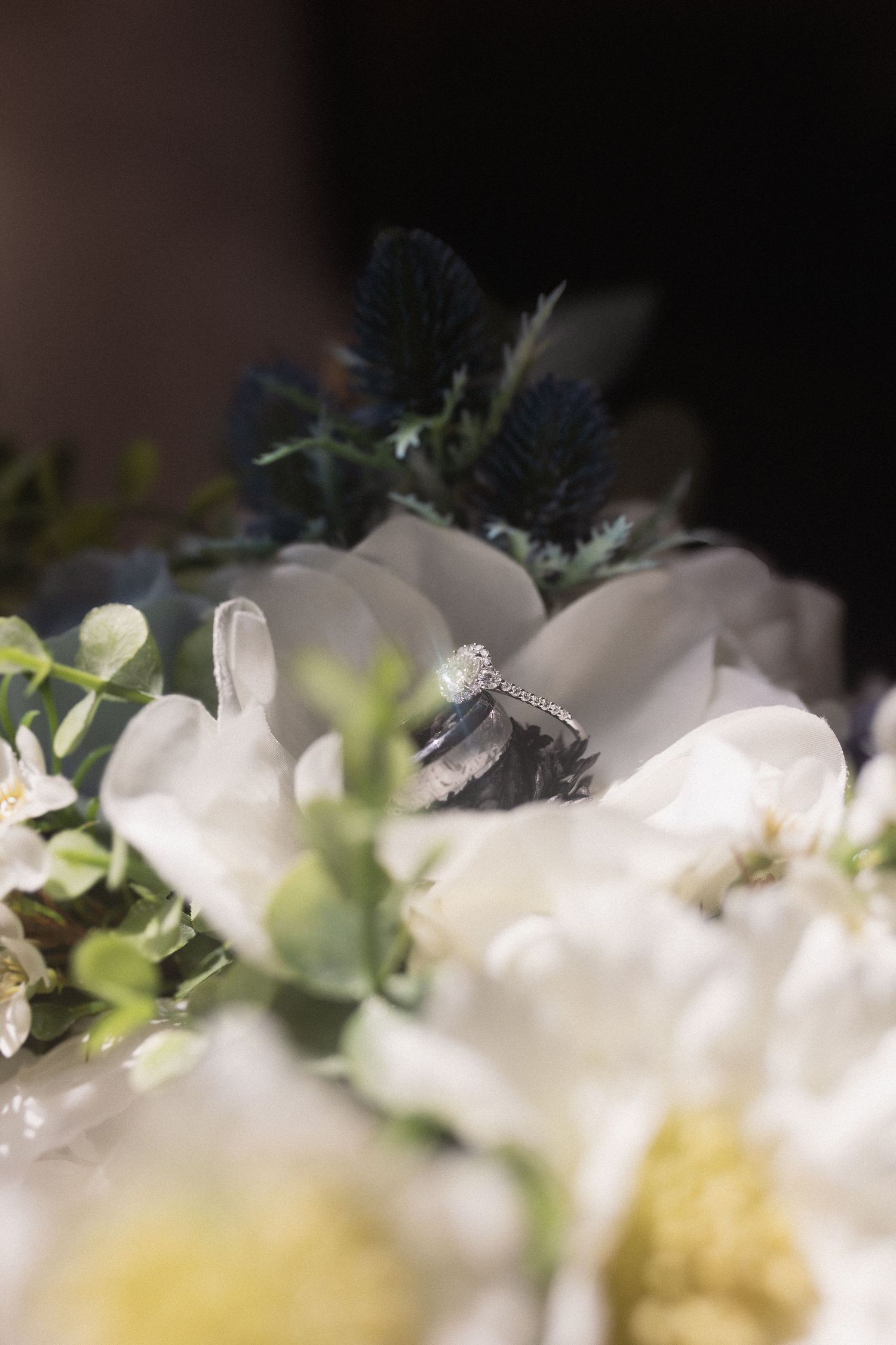 Close up of diamond engagement ring nestled among white flowers and greenery.