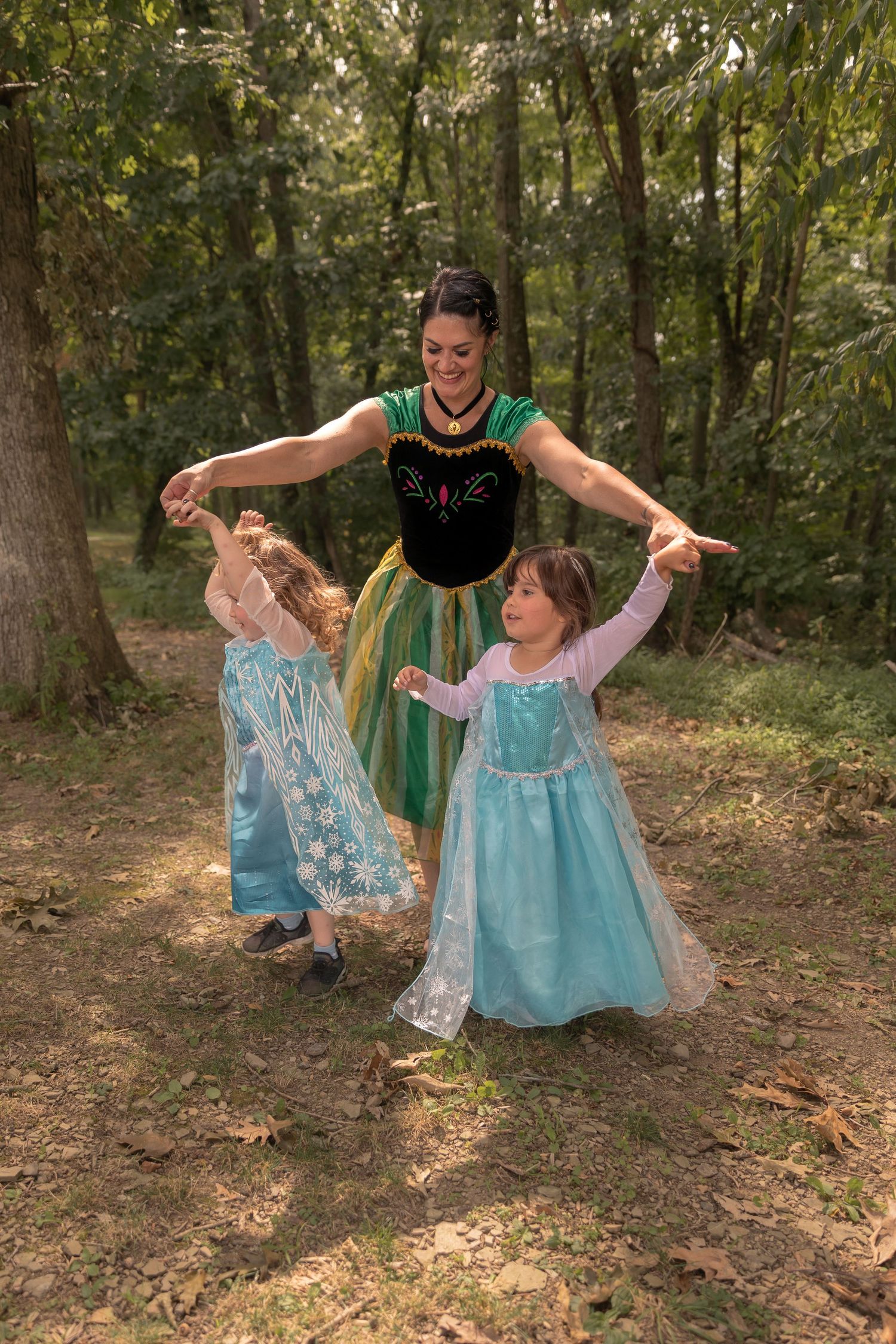 Dancers in colorful princess dresses twirl together in a woodland setting.