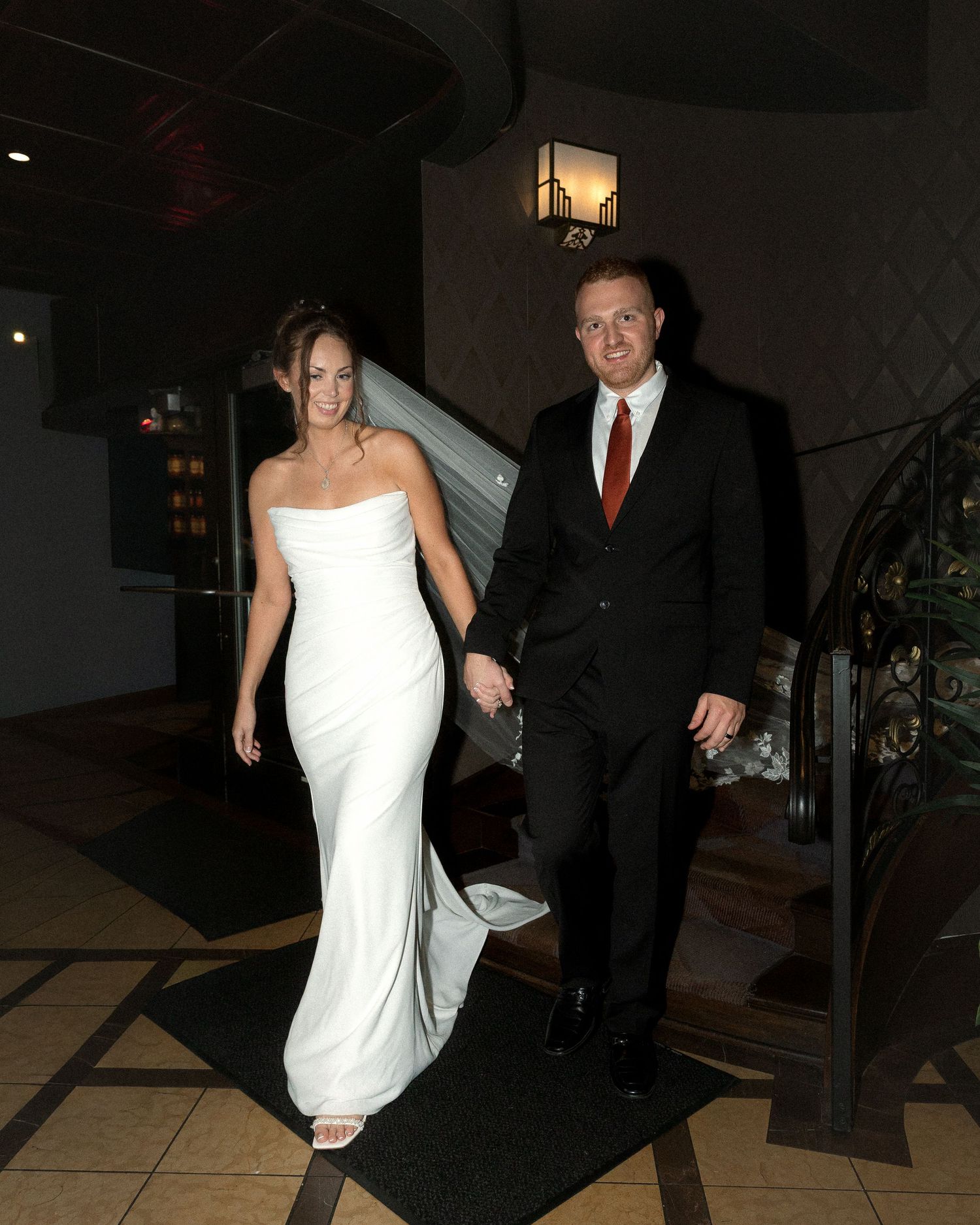 Wedding couple walking together through a dimly lit venue hallway with marble floors.