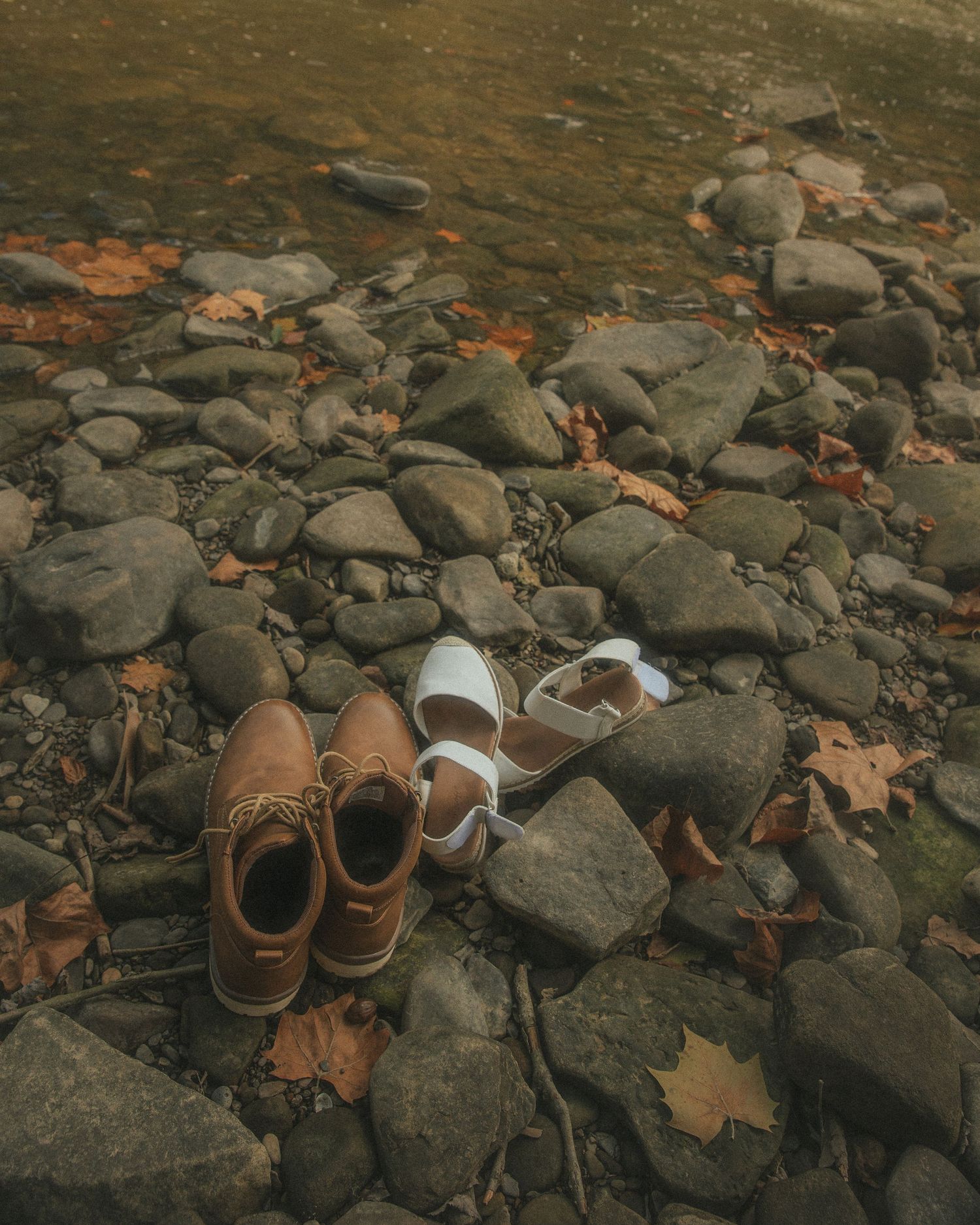 Brown leather shoes and white socks scattered on rocky ground with autumn leaves.
